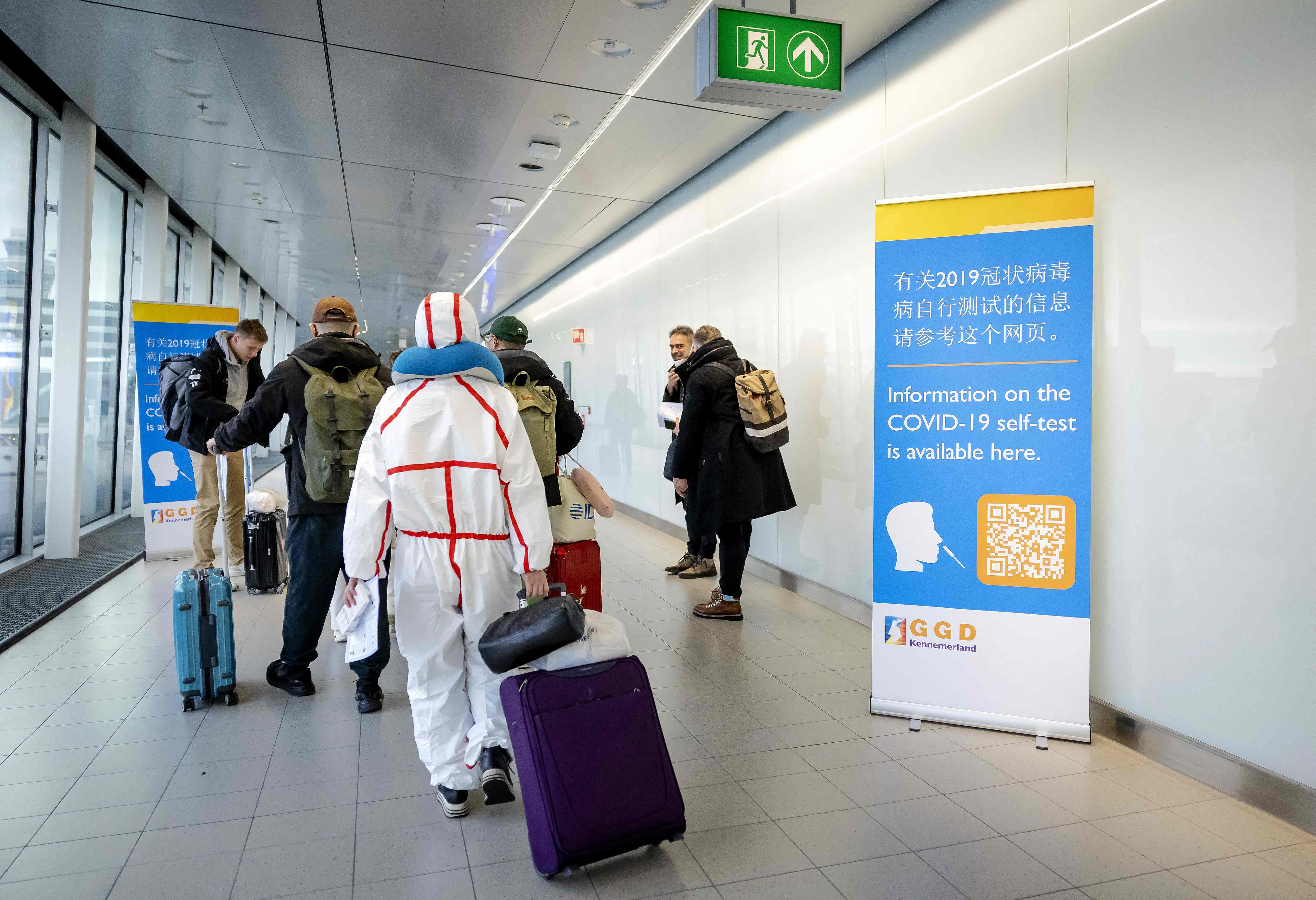 Travelers arriving China walk past information banners and receive free Covid-19 self-test kits, at Amsterdam's Schiphol Airport on January 4, 2023. - More than a dozen countries have imposed coronavirus testing requirements on visitors from China, which is experiencing an explosion of cases after lifting its long-standing zero-Covid measures. (Photo by Robin van Lonkhuijsen / ANP / AFP) / Netherlands OUT