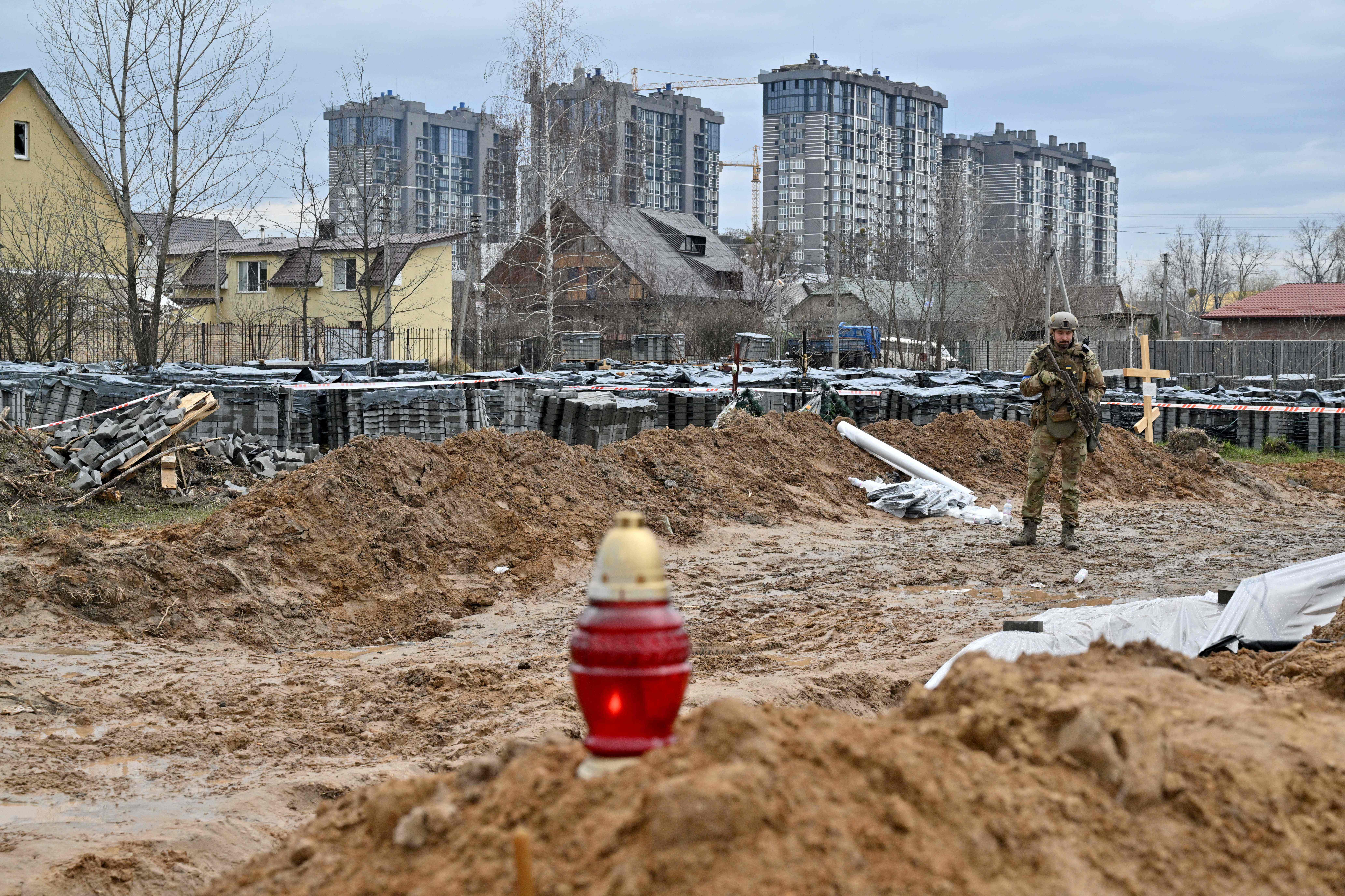 TOPSHOT - A Ukrainian serviceman stands guard near a mass grave in Bucha, near Kyiv on April 9, 2022. (Photo by Sergei SUPINSKY / AFP)
