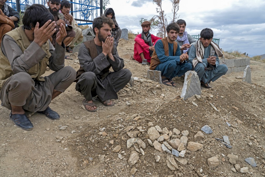 Afghans pray at a grave of victims, after burial ceremony in a cemetery in the outskirts of Kabul on August 18, 2022. - The death toll from a blast which ripped through a mosque packed with worshippers in the Afghan capital Kabul on August 17, has risen to 21, police said. (Photo by Wakil KOHSAR / AFP)