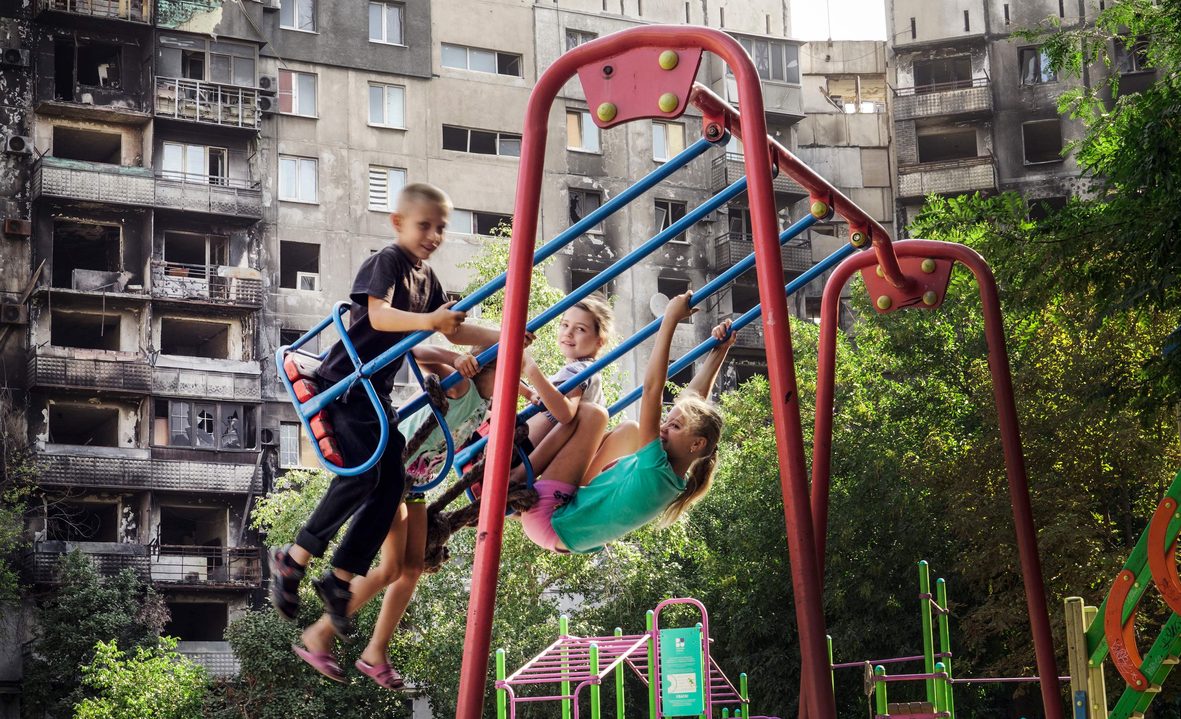 Children play in front of a ruined building in Mariupol on August 28, 2022 amid the ongoing Russian military action in Ukraine. (Photo by STRINGER / AFP)