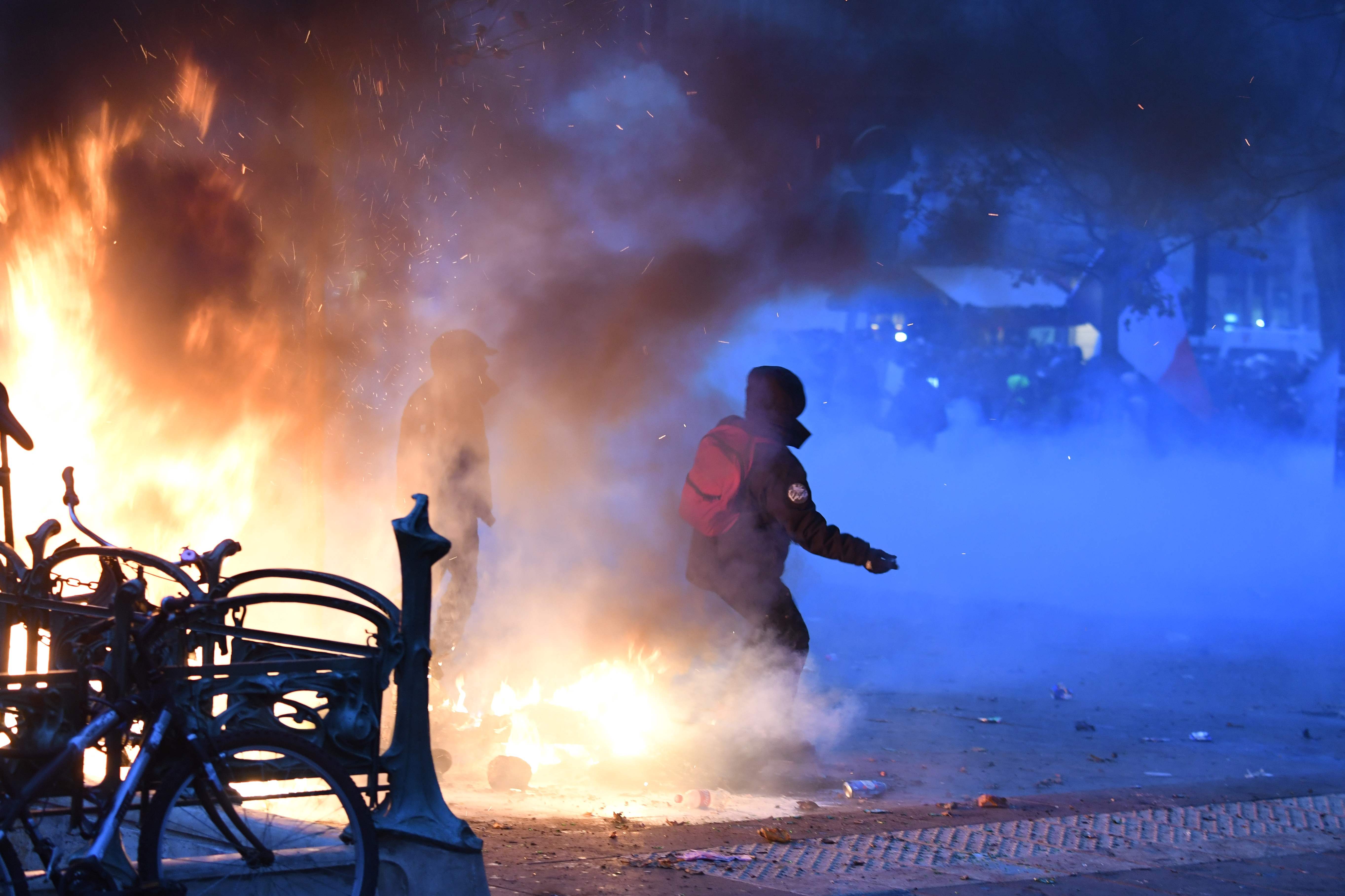 Two protestors stand next to a fire and in tear gas during a demonstration to protest against the pension overhauls, in Paris, on December 5, 2019 as part of a national general strike. - Trains cancelled, schools closed: France scrambled to make contingency plans on for a huge strike against pension overhauls that poses one of the biggest challenges yet to French President's sweeping reform drive. (Photo by Alain JOCARD / AFP)