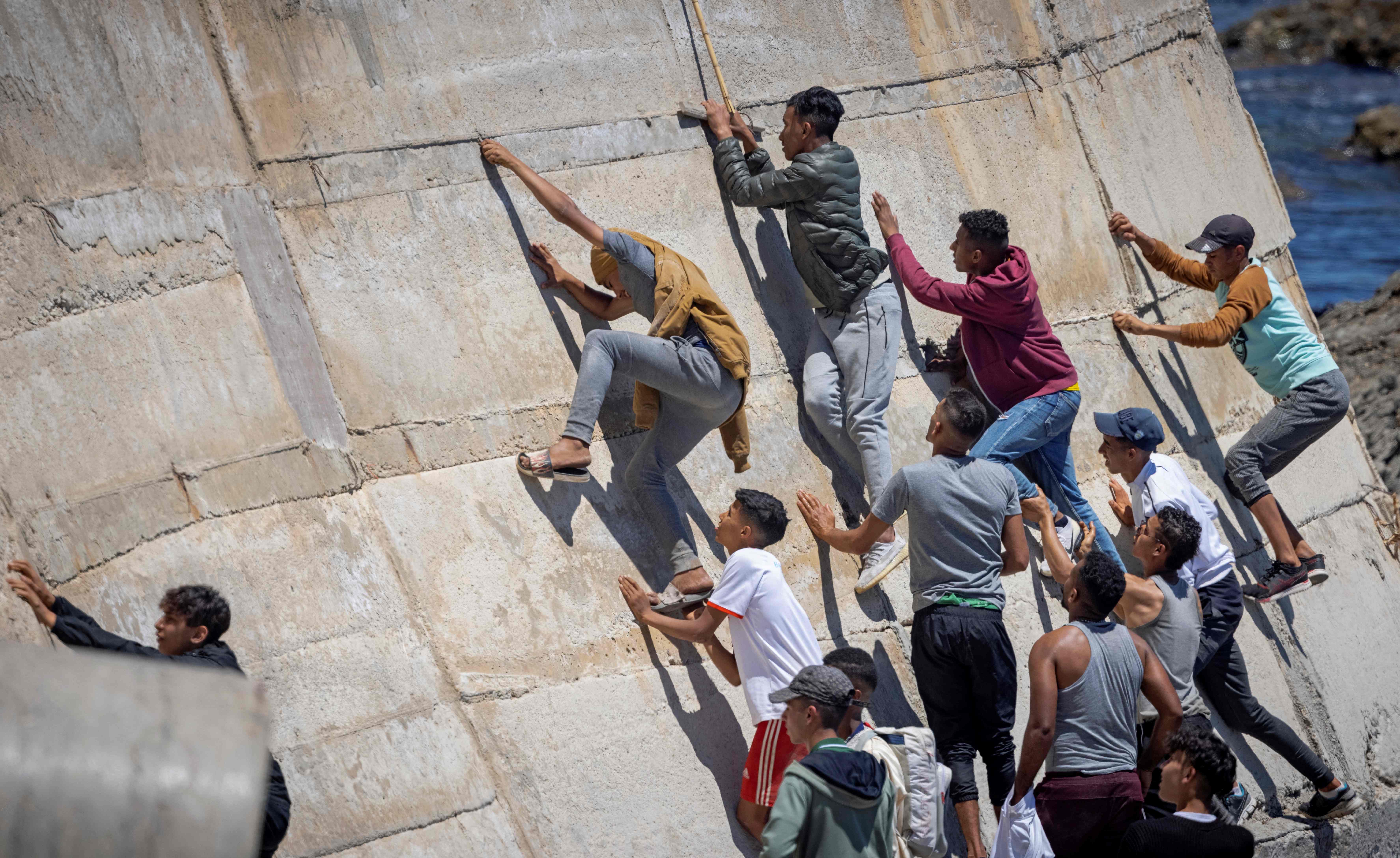 TOPSHOT - Migants climb a sea wall in the northern town of Fnideq after attempting to cross the border from Morocco to Spain's North African enclave of Ceuta on May 19, 2021. - Spain stepped up diplomatic pressure on Rabat as its prime minister flew into Ceuta, vowing to "restore order" in the North African enclave after a record 8,000 migrants reached its beaches from Morocco. (Photo by FADEL SENNA / AFP)