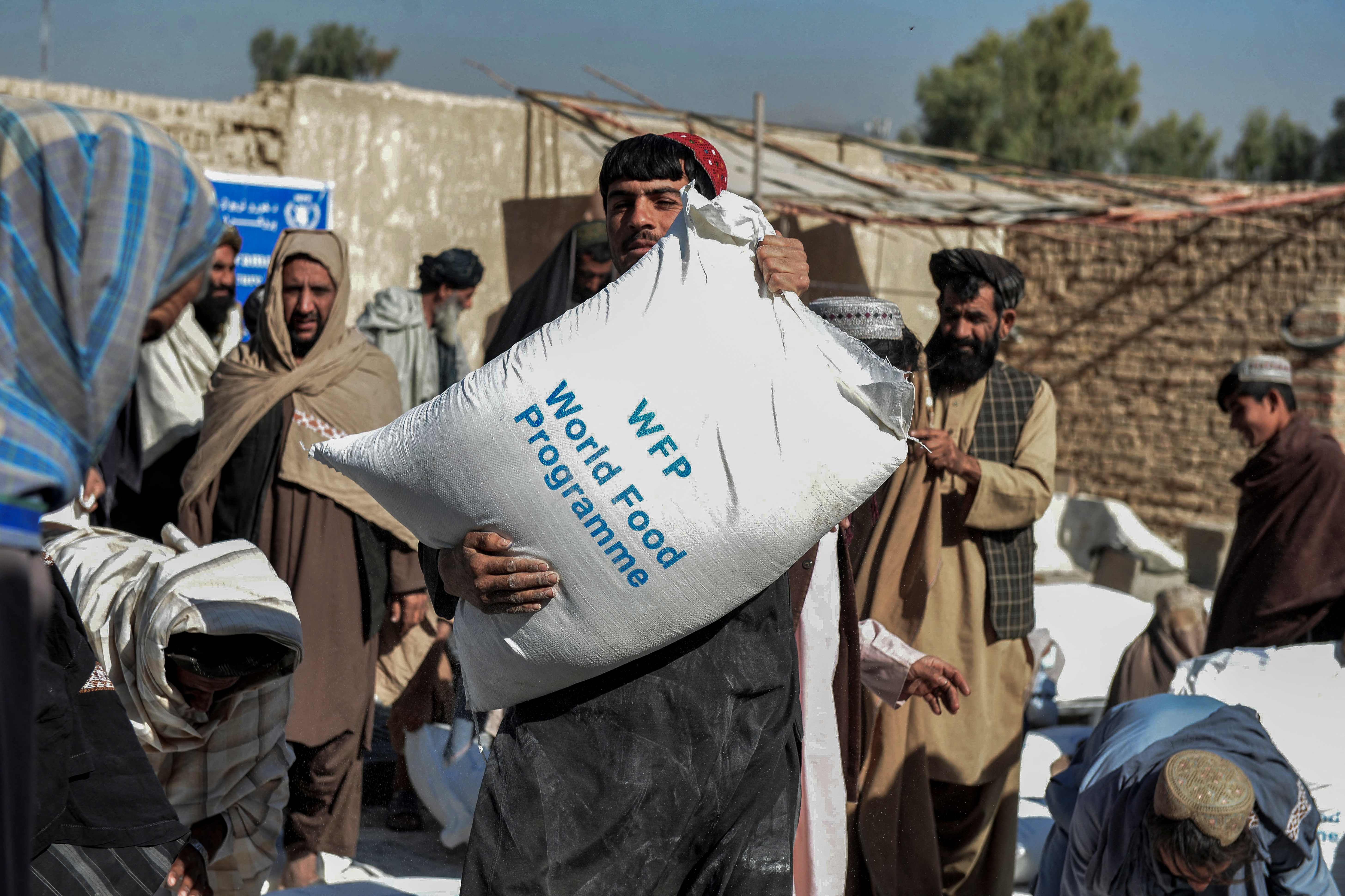 (FILES) In this file photo taken on October 19, 2021 Afghans carry sacks of grains distributed as aid by the World Food Programme in Kandahar, Afghanistan. - The UN Security Council on December 22, 2021, unanimously adopted a US-proposed resolution that facilitates humanitarian aid to Afghanistan, which is on the verge of economic collapse. The resolution states that "payment of funds, other financial assets or economic resources, and the provision of goods and services necessary to ensure the timely delivery of such assistance or to support such activities are permitted." (Photo by Javed TANVEER / AFP)