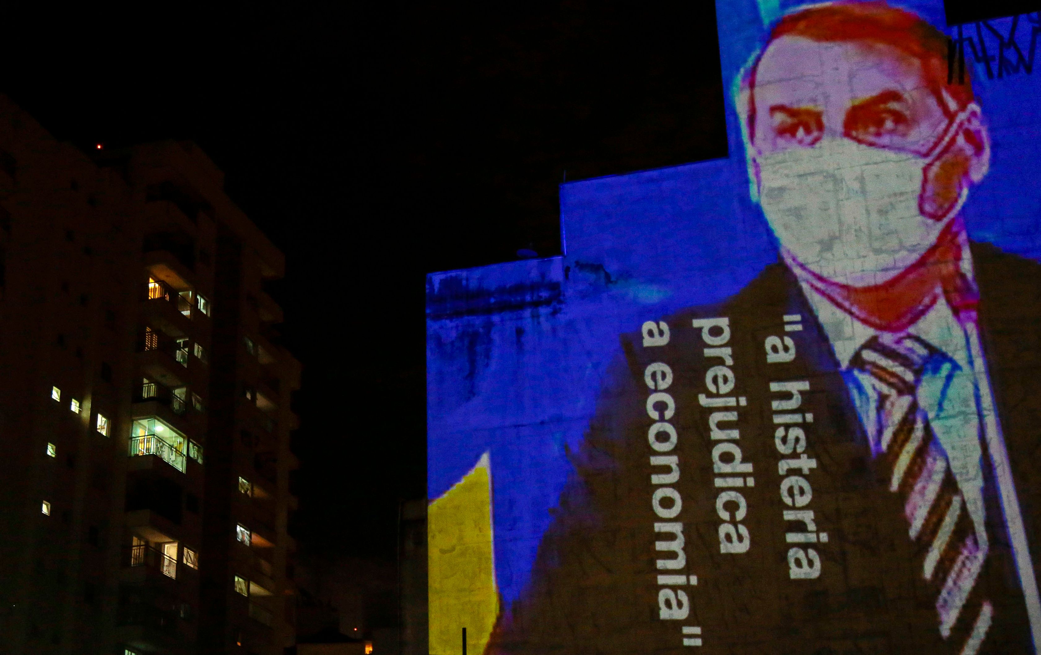 An image of Brazil's President Jair Bolsonaro wearing a protective face mask and the phrase �Hysteria Damages the Economy" is projected on the wall of a building as a protest against the president regarding his handling of the coronavirus COVID-19 outbreak, in Sao Paulo, Brazil, March 21, 2020. - An estimated 900 million people are now confined to their homes in 35 countries around the world -- including 600 million hemmed in by obligatory government lockdown orders -- according to an AFP tally on March 21 at 1900 GMT based on official sources. (Photo by Miguel SCHINCARIOL / AFP)