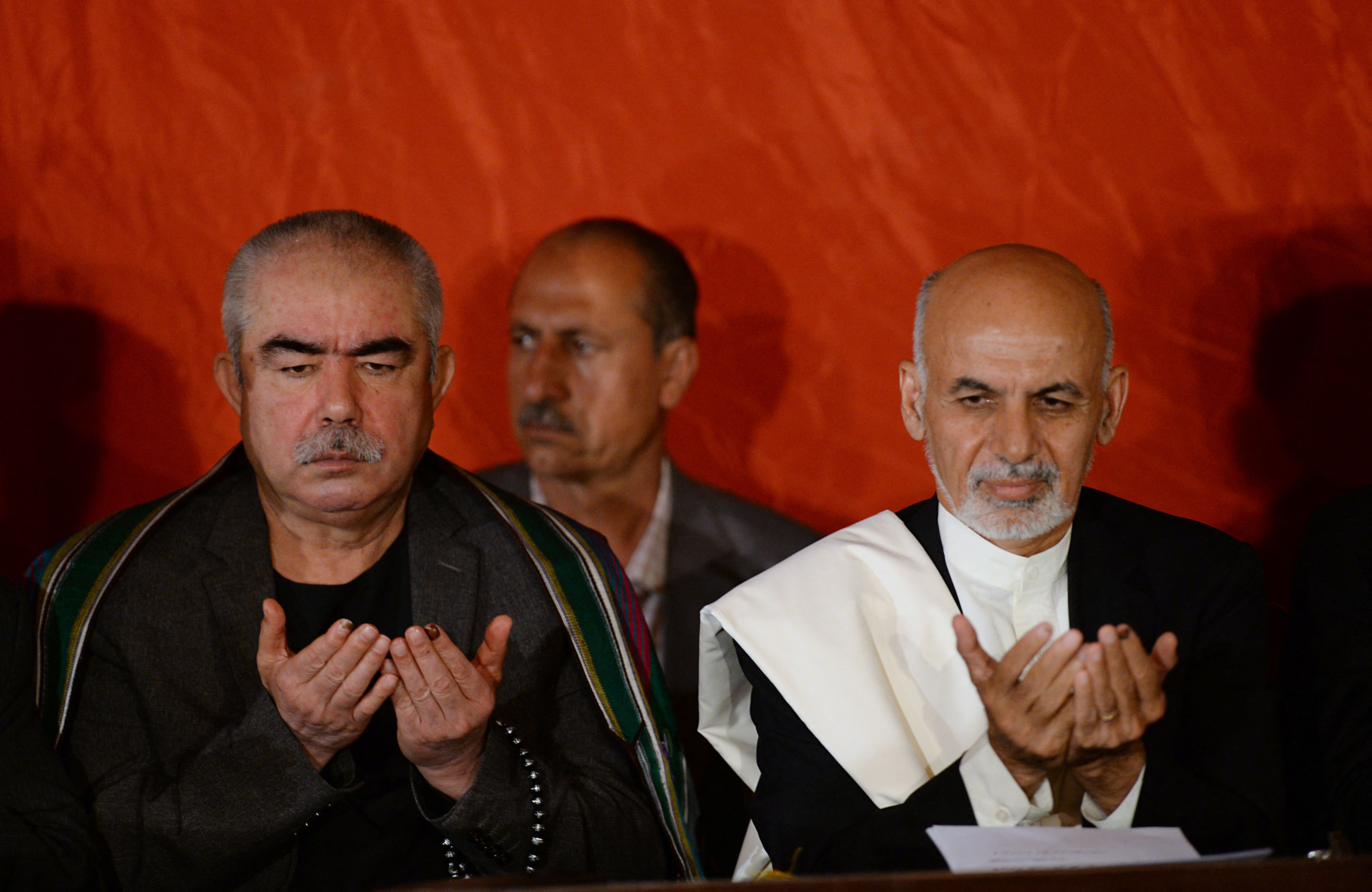 (FILES) In this file photo taken on June 25, 2014, Afghan presidential candidate Ashraf Ghani (R) and his vice-presidential candidate former warlord Abdul Rashid Dostum (L) pray during a press conference at his residence in Kabul. - The scene was a familiar one as warlord Abdul Rashid Dostum jetted into northern Afghanistan this week -- a promise of bloodshed and vengeance, and no apology for his vicious past. (Photo by SHAH MARAI / AFP)