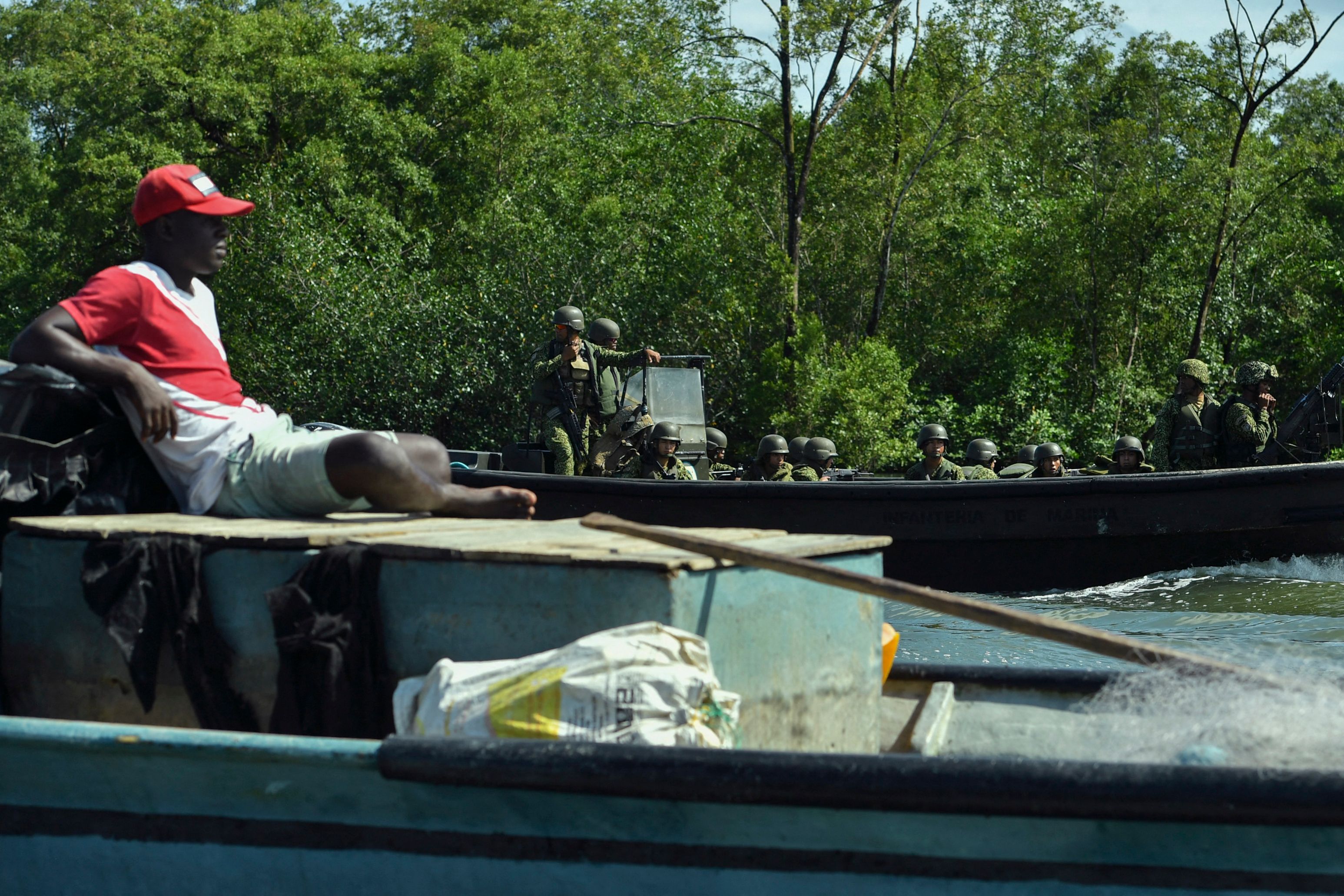 A fisherman rests next to members of the Colombian Navy patrolling on a boat in Buenaventura, Colombia, on September 3, 2022. - Most of Buenaventura is controled by local gangs that dispute the territory with violence and illegal economies like drug trafficking and extorsion. (Photo by JOAQUIN SARMIENTO / AFP)