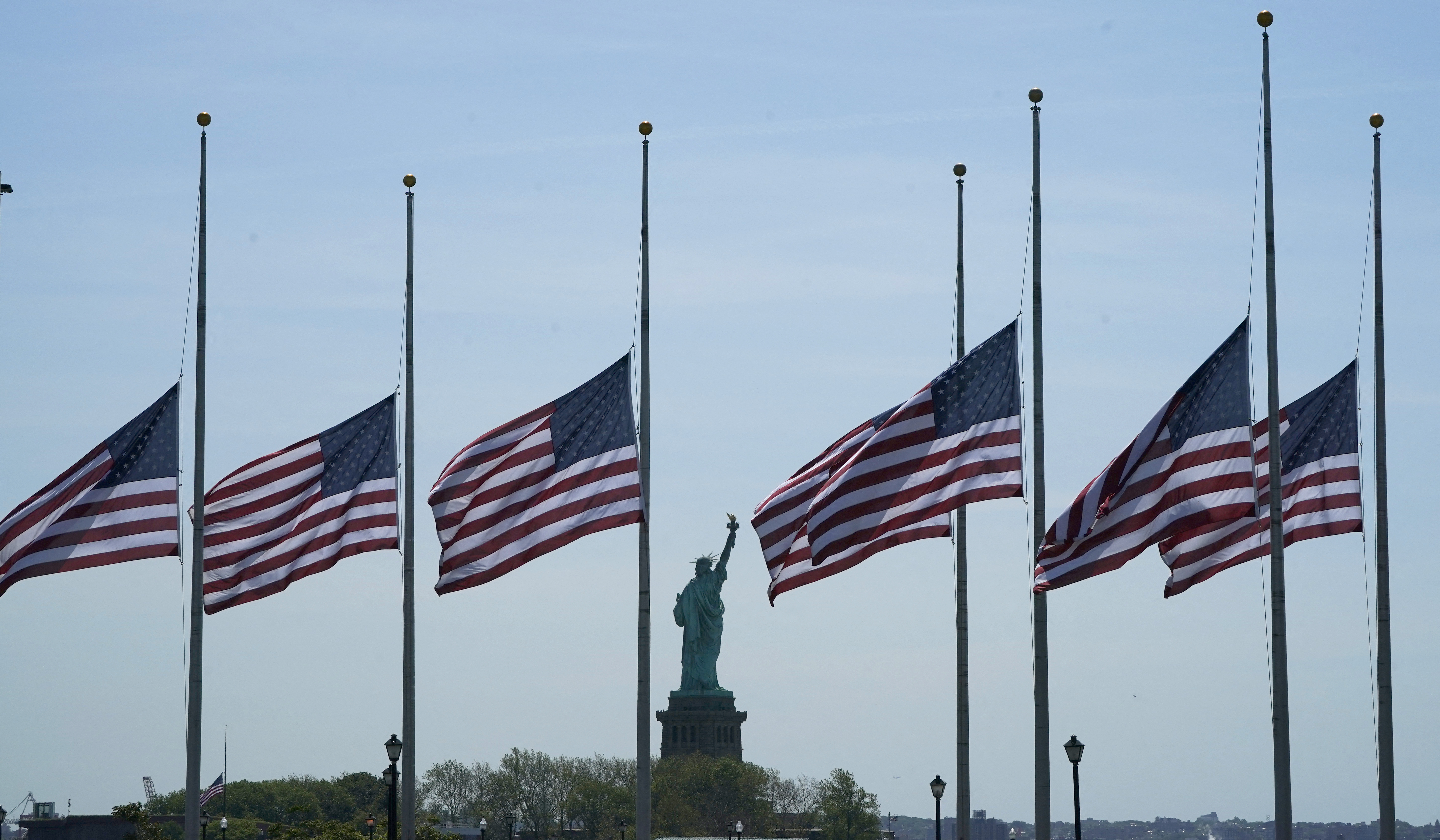 US flags, across New York Bay from the Statue of Liberty, fly at half-mastat Liberty State Park in Jersey City, New Jersey, on May 25, 2022, as a mark of respect for the victims of the May 24 shooting at Robb Elementary School in Uvalde, Texas. - A teenage gunman killed at least 19 young children and two teachers at the elementary school on May 24, prompting President Joe Biden to denounce the US gun lobby and vow to end the nation's cycle of mass shootings. (Photo by TIMOTHY A. CLARY / AFP)