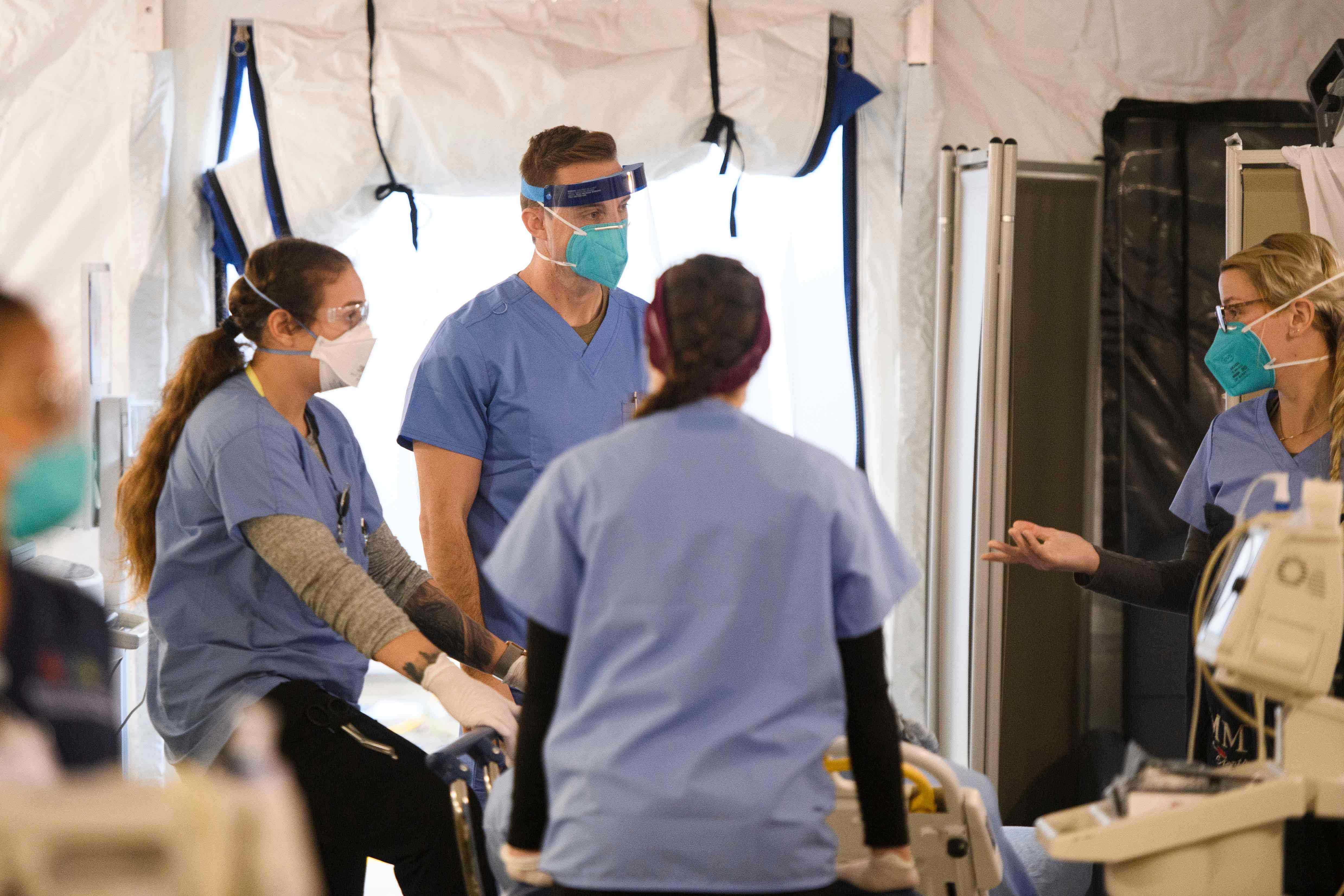 A California National Guard nurse (C) wears personal protective equipment (PPE) while working hospital staff to assist patients in a suspected Covid-19 patient triage area set up in a field hospital tent outside the emergency department of Martin Luther King Jr. (MLK) Community Hospital on January 6, 2021 in the Willowbrook neighborhood of Los Angeles, California. - Deep within a South Los Angeles hospital, a row of elderly Hispanic men in induced comas lay hooked up to ventilators, while nurses clad in spacesuit-looking respirators checked their bleeping monitors in the eerie silence. The intensive care unit in one of the city's poorest districts is well accustomed to death, but with Los Angeles now at the heart of the United States' Covid pandemic, medics say they have never seen anything on this scale. (Photo by Patrick T. FALLON / AFP)