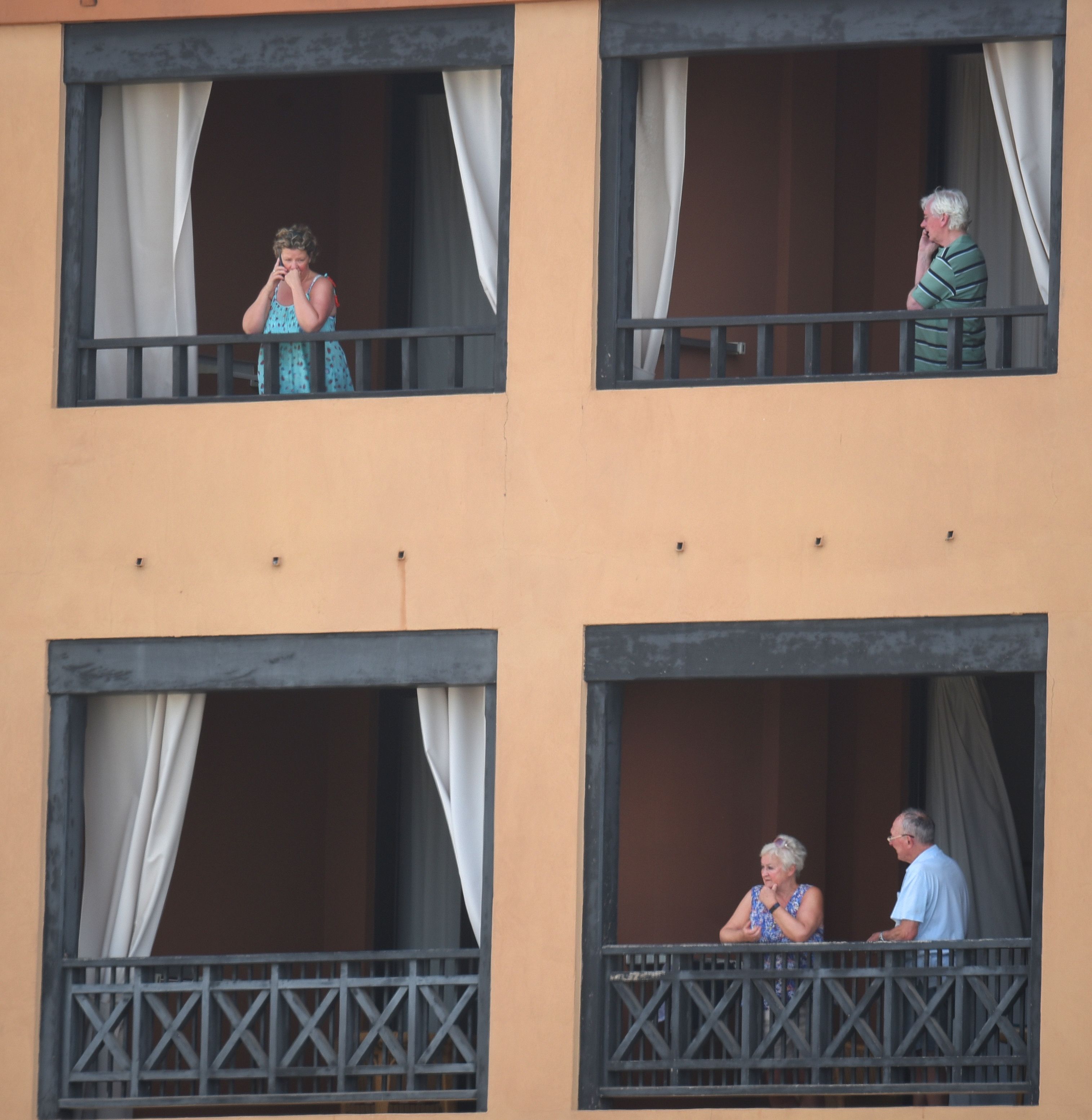 Tourists stand on the balcony of their rooms at the H10 Costa Adeje Palace Hotel in La Caleta, on February 25, 2020, where hundreds of people were confined to their rooms after an Italian tourist was hospitalised with a suspected case of coronavirus. - Tourists staying in a four-star hotel on the Spanish island of Tenerife, in the Canary archipielago, were confined to their rooms today following the announcement of a suspected novel coronavirus, COVID-19, case waiting for official confirmation. This possible case was detected yesterday in Tenerife, where an Italian national passed a first test which turned out to be positive, announced the Spanish Ministry of Health. (Photo by DESIREE MARTIN / AFP)