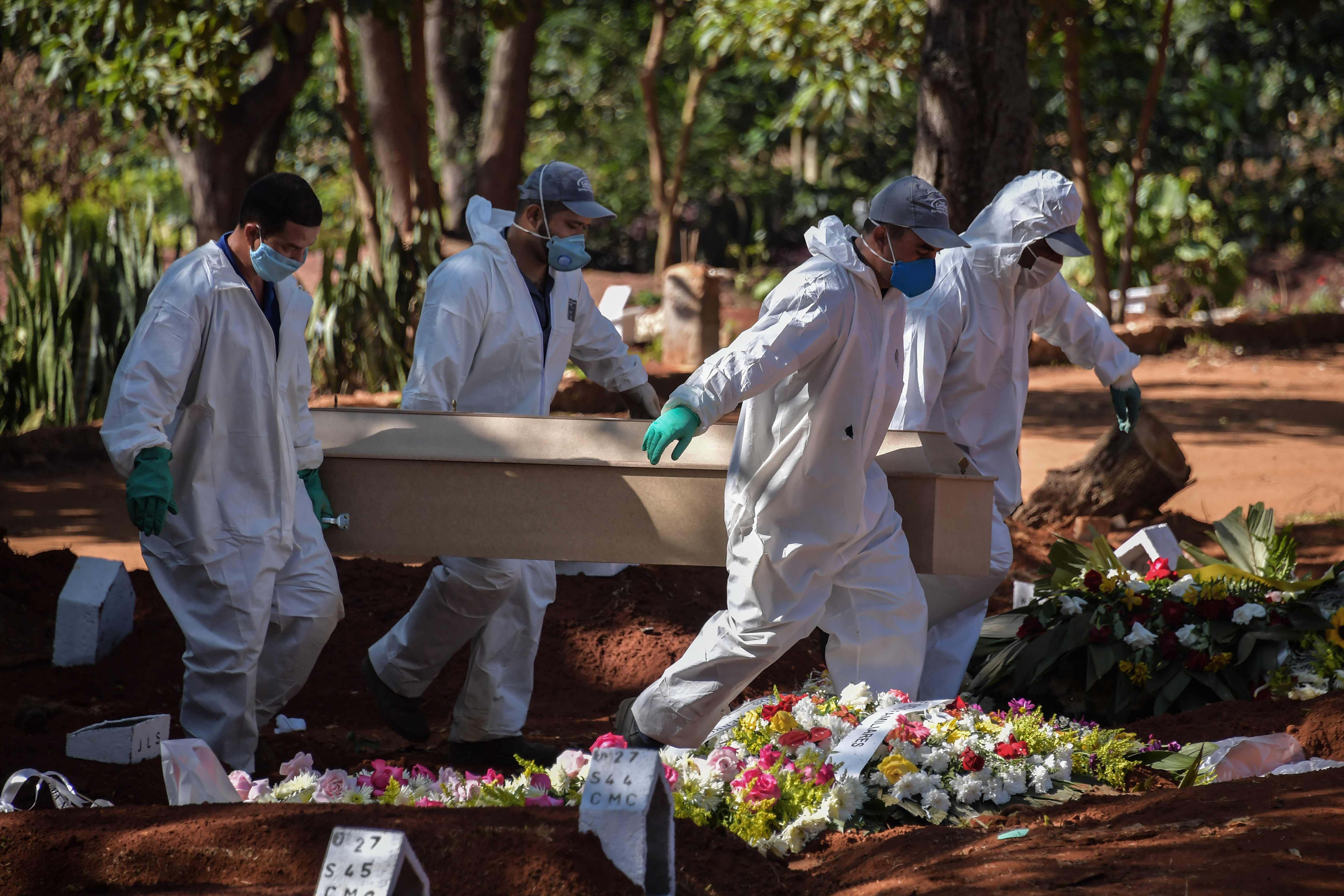 TOPSHOT - Employees carry the coffin of a person who died from COVID-19 at the Vila Formosa cemetery, in the outskirts of Sao Paulo, Brazil on May 20, 2020. - Brazil has emerged as the latest flashpoint in the coronavirus pandemic. The country has registered more than 270,000 cases and nearly 18,000 deaths so far, and the increase in infections is not expected to peak until June. (Photo by NELSON ALMEIDA / AFP)