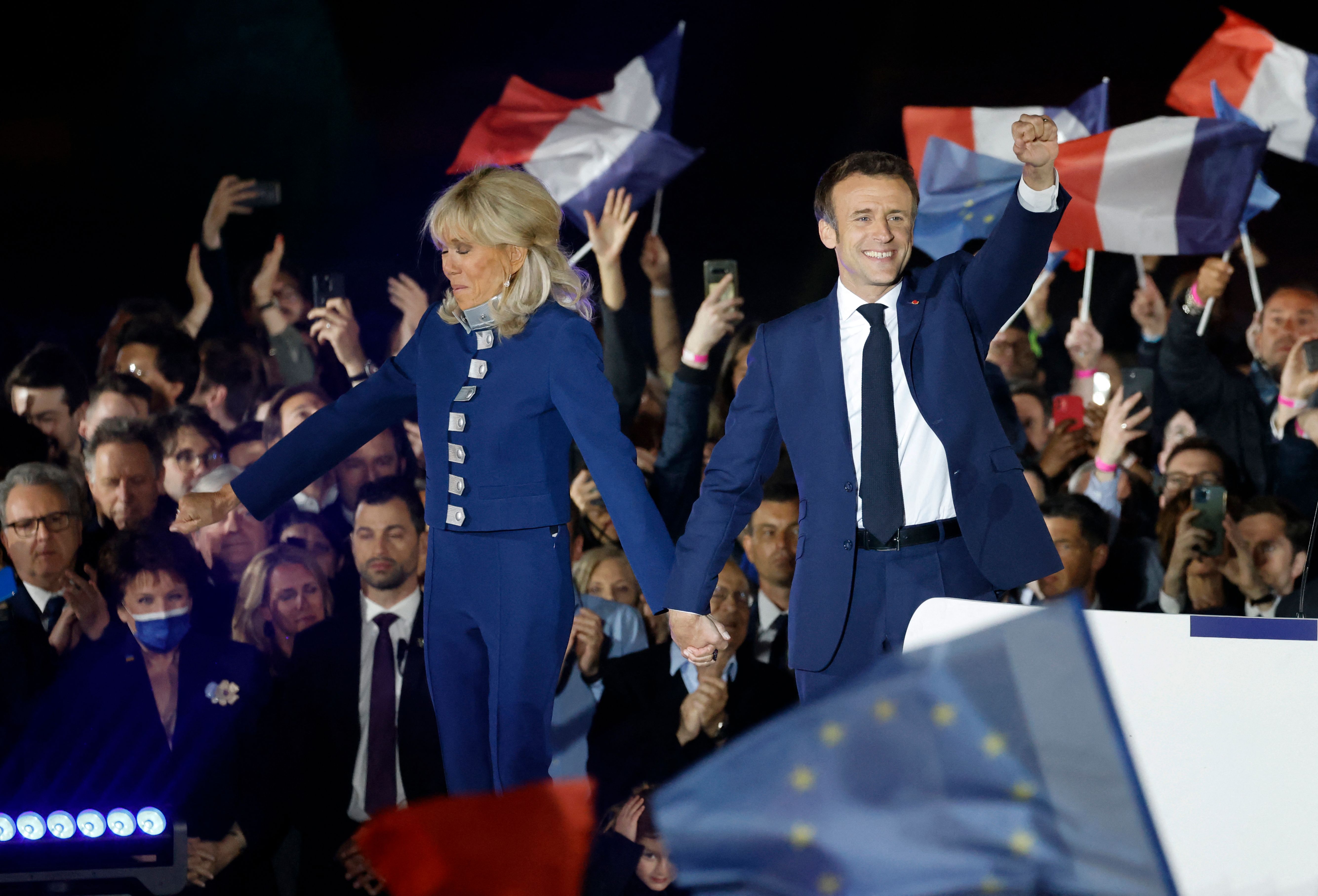 TOPSHOT - French President and La Republique en Marche (LREM) party candidate for re-election Emmanuel Macron (R) holds his fist in the air as he holds Brigitte Macron's hand after his victory in France's presidential election, at the Champ de Mars in Paris, on April 24, 2022. (Photo by Ludovic MARIN / AFP)