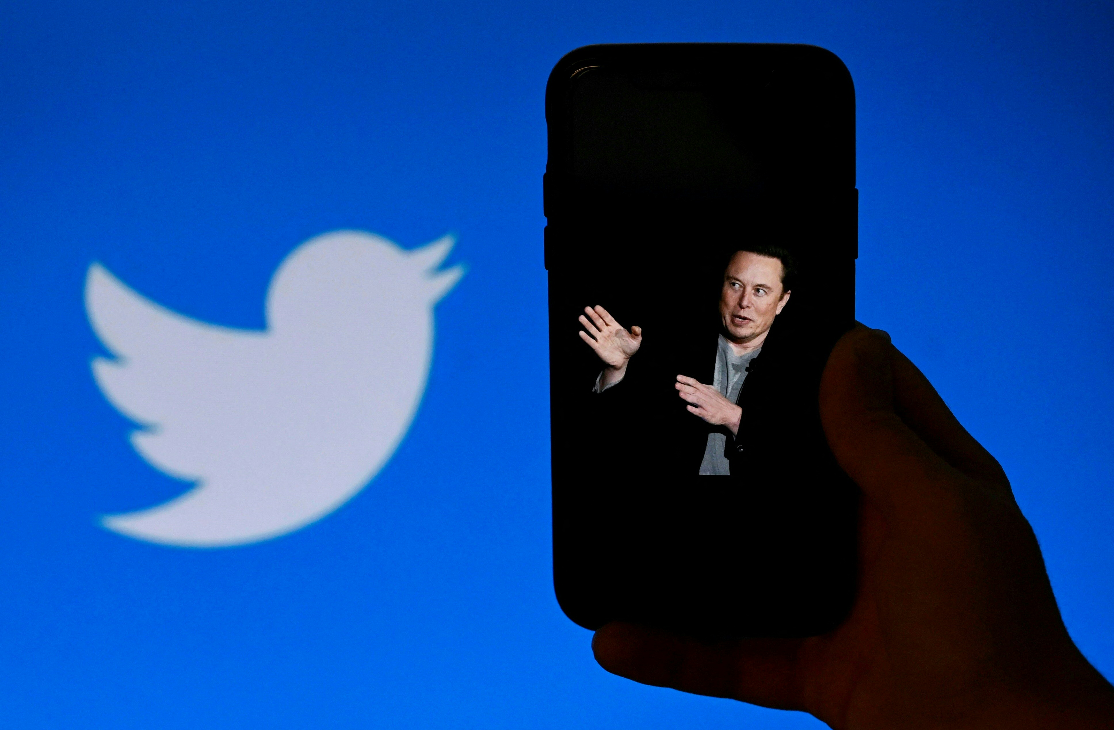 In this photo illustration, a phone screen displays a photo of Elon Musk with the Twitter logo shown in the background, on October 4, 2022, in Washington, DC. - Elon Musk has offered to push through with his buyout of Twitter at the original agreed price, reports said Tuesday, prompting a surge in the share price of the social network that triggered a suspension of trading. (Photo by OLIVIER DOULIERY / AFP)