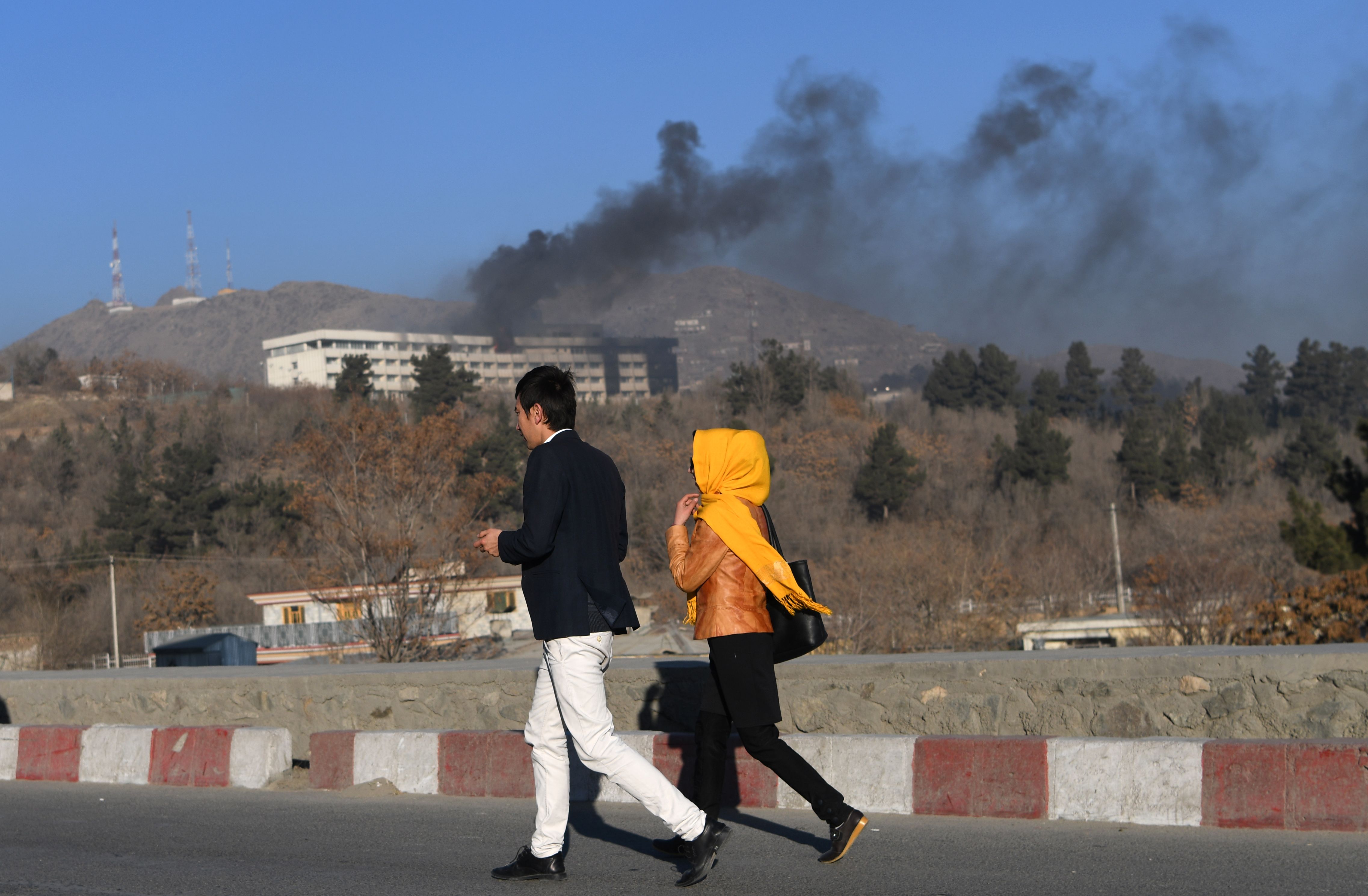 TOPSHOT - Afghans walk near the Intercontinental Hotel as smoke billows during a fight between gunmen and Afghan security forces in Kabul on January 21, 2018.
Gunmen stormed a luxury hotel in Kabul killing at least six people, including a foreigner, sparking a twelve hour fight with security forces that left terrified guests scrambling to escape and parts of the building ablaze. Afghan security forces killed four attackers during the night-time siege, interior ministry spokesman Najib Danish told Tolo News, during which people trapped inside the landmark hotel were seen climbing over balconies to escape.
/ AFP PHOTO / WAKIL KOHSAR