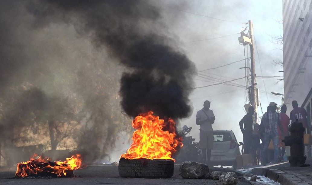 TOPSHOT - This screen grab taken from AFPTV shows tires on fire near the main prison of Port-au-Prince, Haiti, on March 3, 2024, after a breakout by several thousand inmates. At least a dozen people died as gang members attacked the main prison in Haiti's capital, triggering a breakout by several thousand inmates, an AFP reporter and an NGO said on March 3. "We counted many prisoners' bodies," said Pierre Esperance of the National Network for Defense of Human Rights, adding that only around 100 of the National Penitentiary's estimated 3,800 inmates were still inside the facility after the gang assault overnight on March 2. (Photo by Luckenson JEAN / AFPTV / AFP)