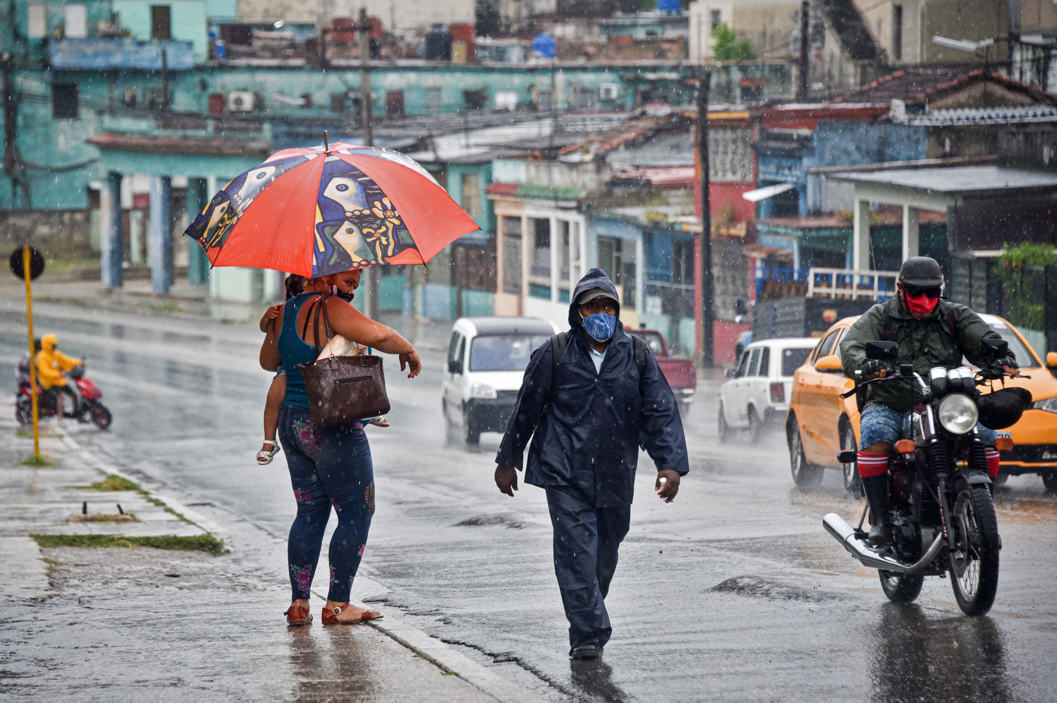 People walk under the rain in Havana on August 27, 2021, as Hurricane Ida passes through eastern Cuba. - Storm Ida has strengthened into a hurricane as it barrels toward Cuba and the US Gulf Coast, the National Hurricane Center said Friday. (Photo by ADALBERTO ROQUE / AFP)