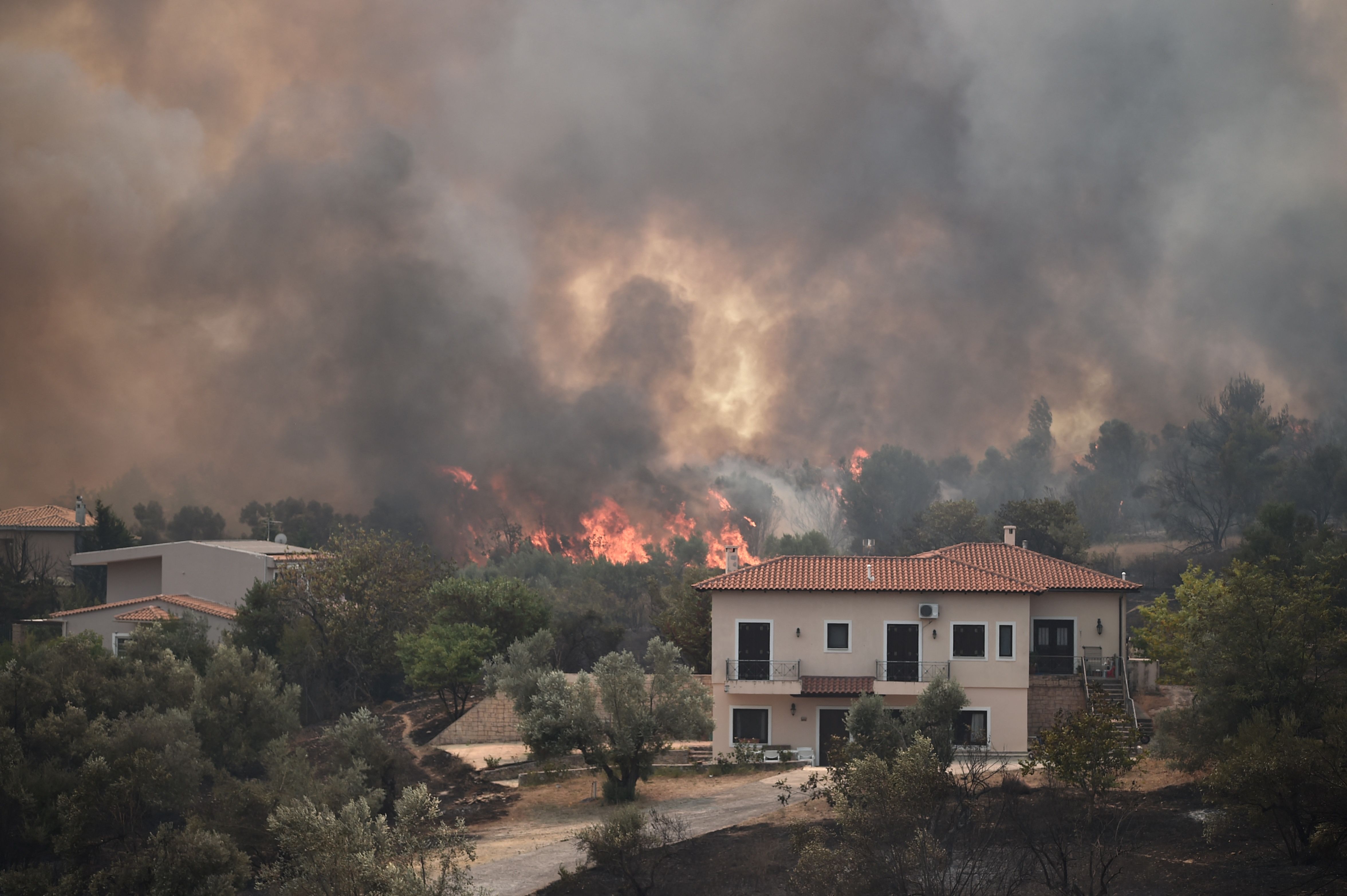 TOPSHOT - A picture taken on August 6, 2021 shows flames near houses as a fire spreads in the village of Afidnes, some 30 kilometres north of Athens. - Hundreds of firefighters battled a blaze on the outskirts of Athens on August 6 as dozens of fires raged in Greece. (Photo by Louisa GOULIAMAKI / AFP)
