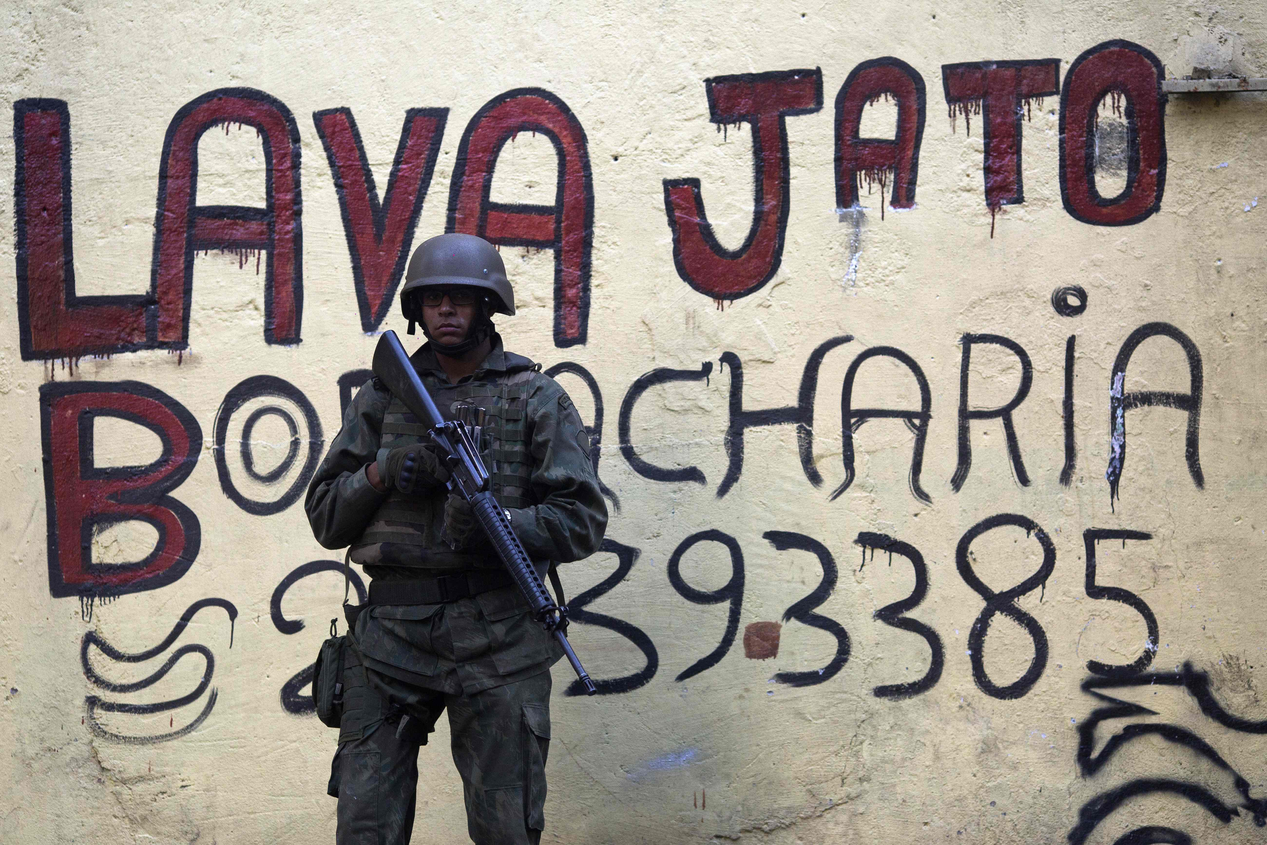 (FILES) In this file photo taken on September 26, 2017 a Brazilian soldier stands guard in front of a graffiti ardvertising a car wash (Lava Jato), the name of the anticorruption operation that shook up the country, during an operation in the Rocinha favela in Rio de Janeiro, Brazil. - One of the biggest corruption investigations in history, Brazil's "Operation Car Wash," which felled presidents and powerful players across Latin America, wrapped up this week after falling into scandal itself. (Photo by Mauro PIMENTEL / AFP)