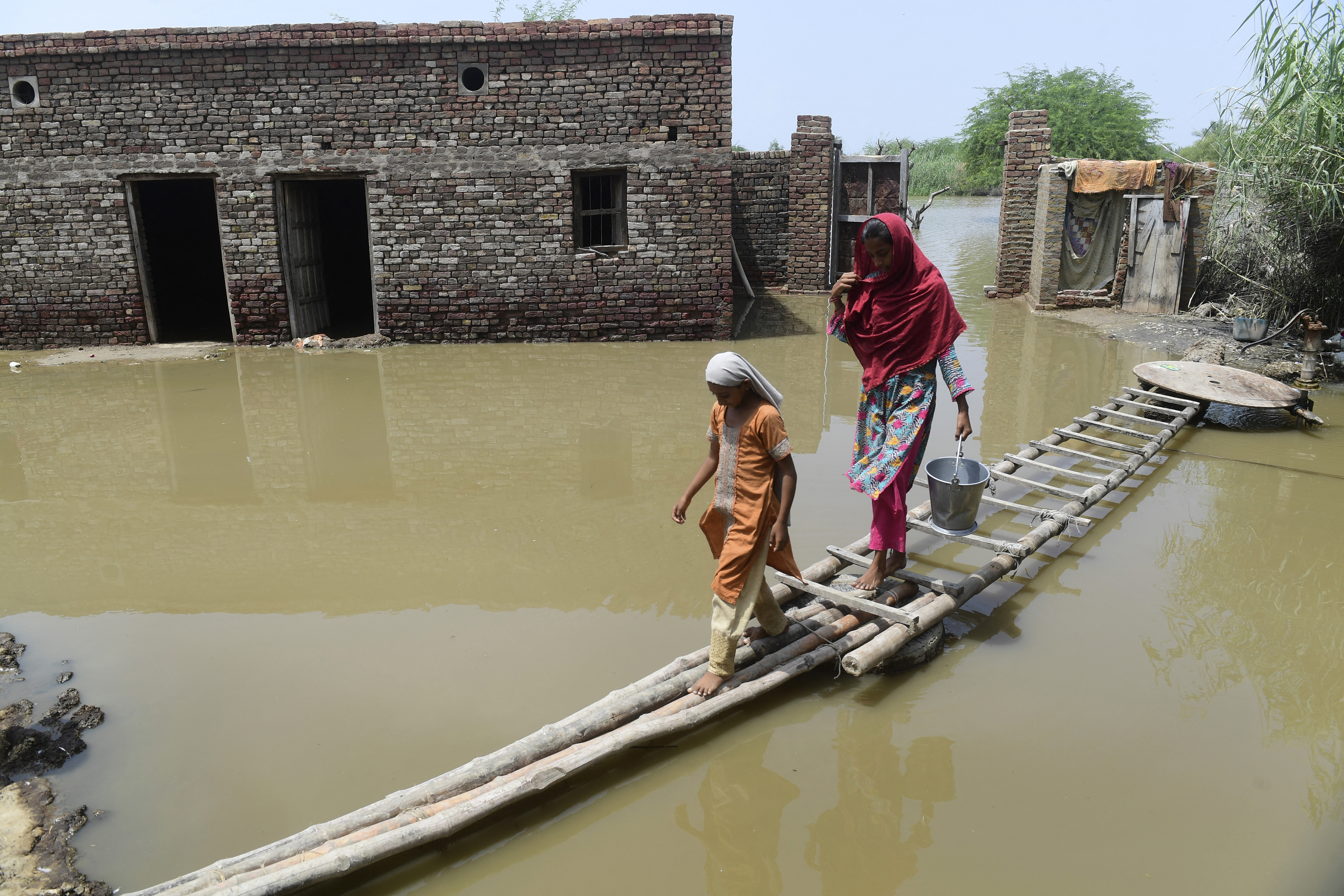 Flood affected people walk on a temporary bamboo path near their flooded house in Shikarpur of Sindh province on August 29, 2022. - The death toll from monsoon flooding in Pakistan since June has reached 1,136, according to figures released on August 29 by the country's National Disaster Management Authority. (Photo by Asif HASSAN / AFP)