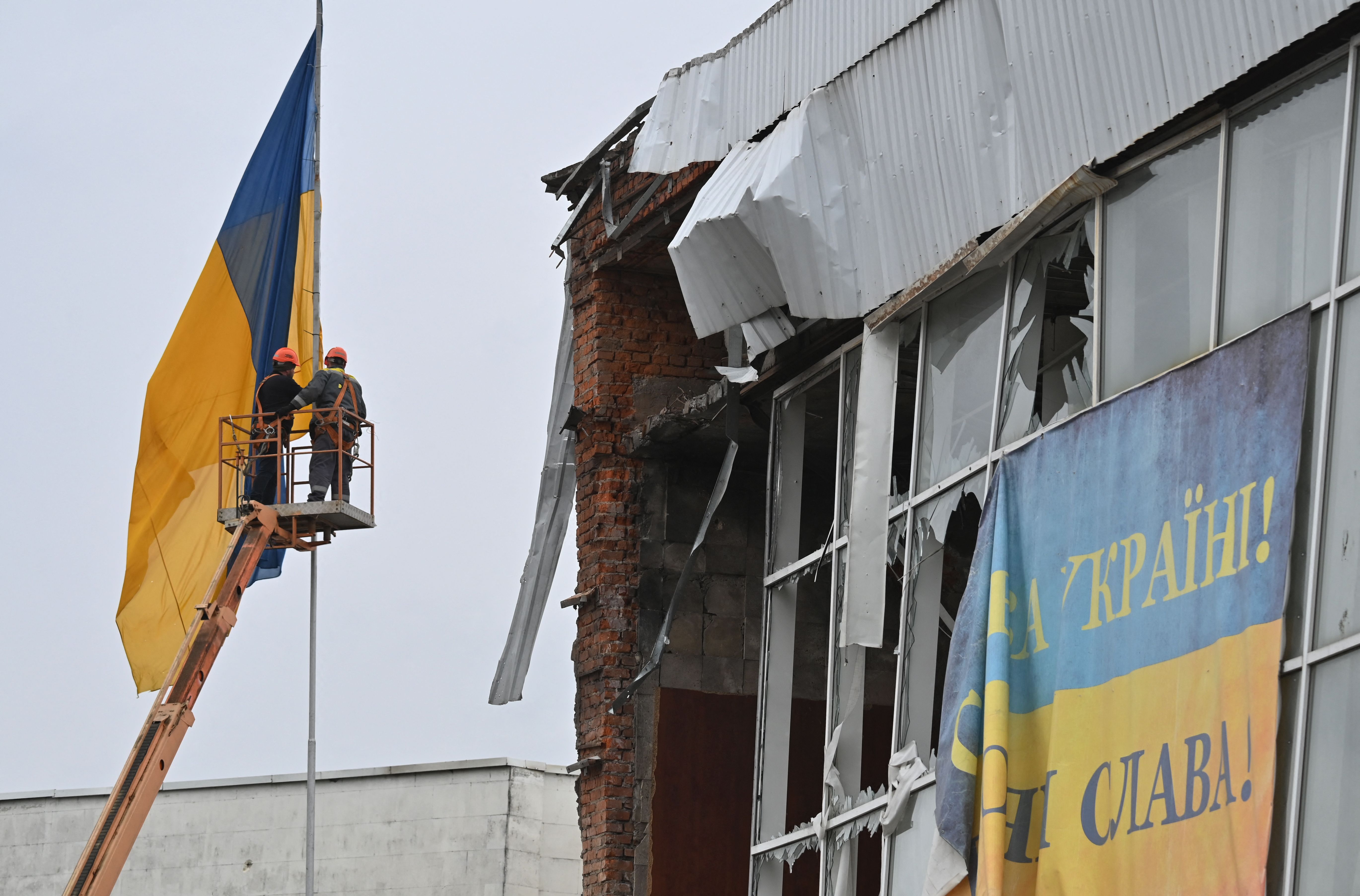 Workers put an Ukrainian flag on a flagpole at a destroyed building in the centre of Makariv, Kyiv region, on April 10, 2022, during the Russian invasion of Ukraine. (Photo by Sergei SUPINSKY / AFP)