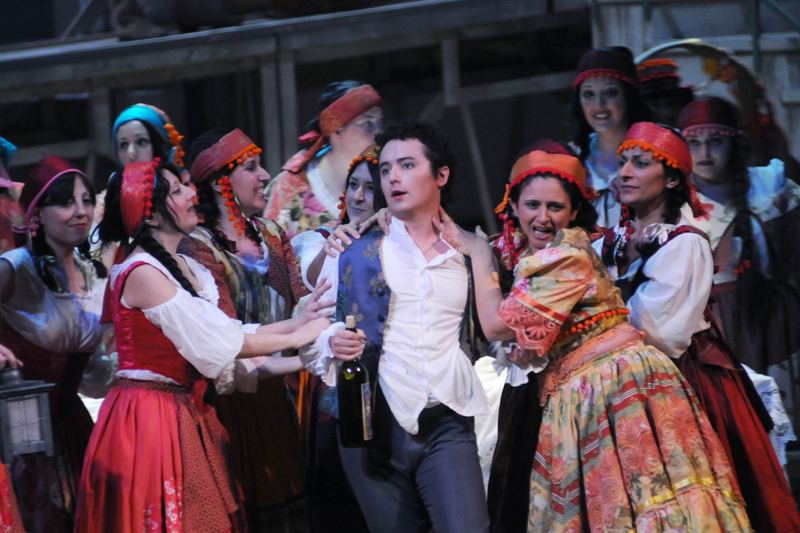 Escena de L’elisir d’amore en el Teatro Verdi de Salerno ( Italia), ofrecida bajo la dirección de Michele Mirabella. Casi al final de la obra, Nemorino –con la botella del elíxir en la mano– es asediado por las jóvenes del pueblo.