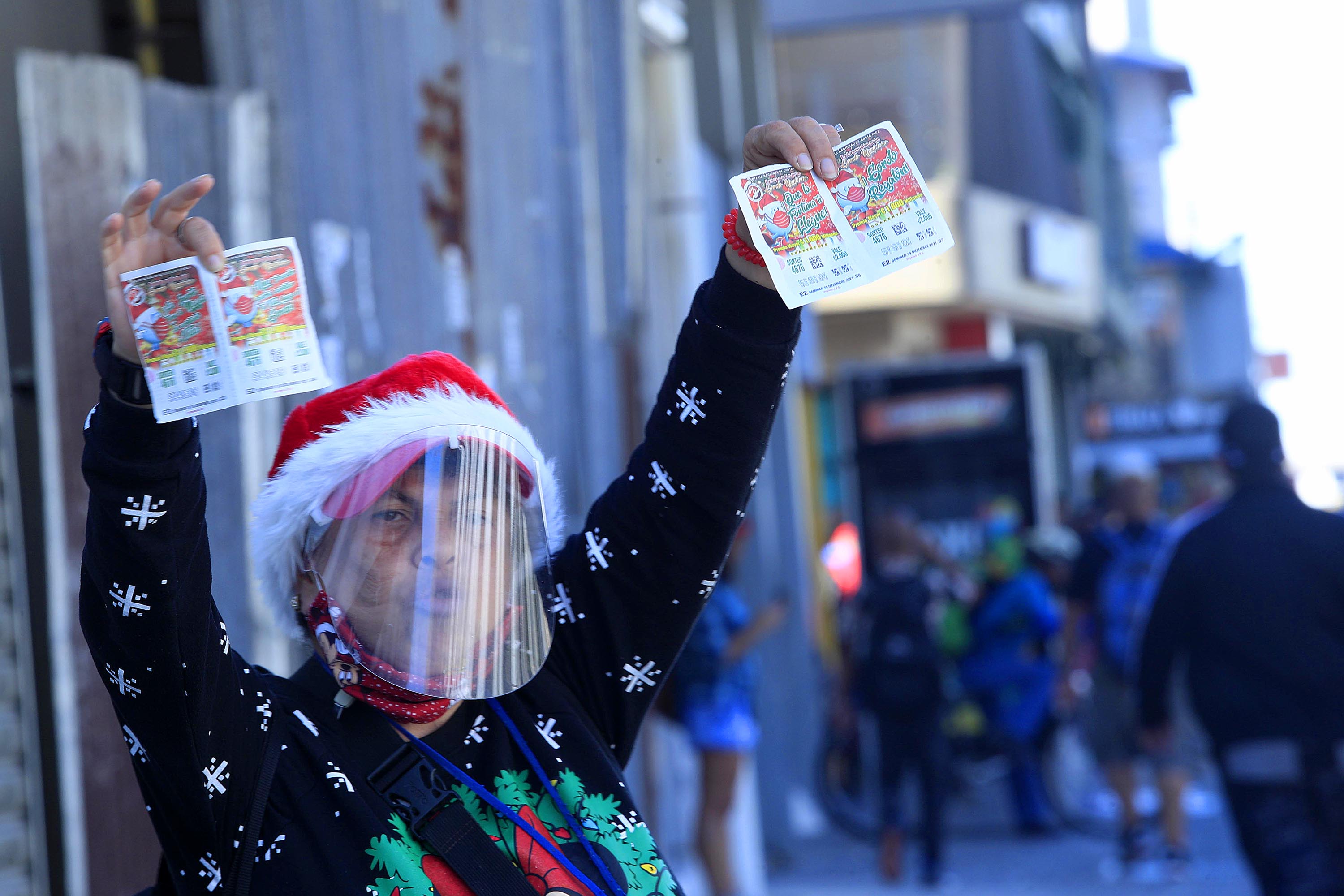 14/11/2021 San José. Ana María Mendoza Aguilar, 65 años, vende lotería frente al costado sur de la Catedral Metropolitana. Usa un una suéter y gorro navideños y la mesita la tiene decorada con botas navideñas.