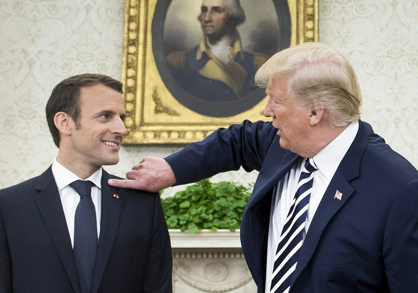 El presidente estadounidense, Donald Trump (der.) despeja una basura del hombro del presidente francés, Emmanuel Macron, en la Oficina Oval antes de una reunión en la Casa Blanca, el 24 de abril.