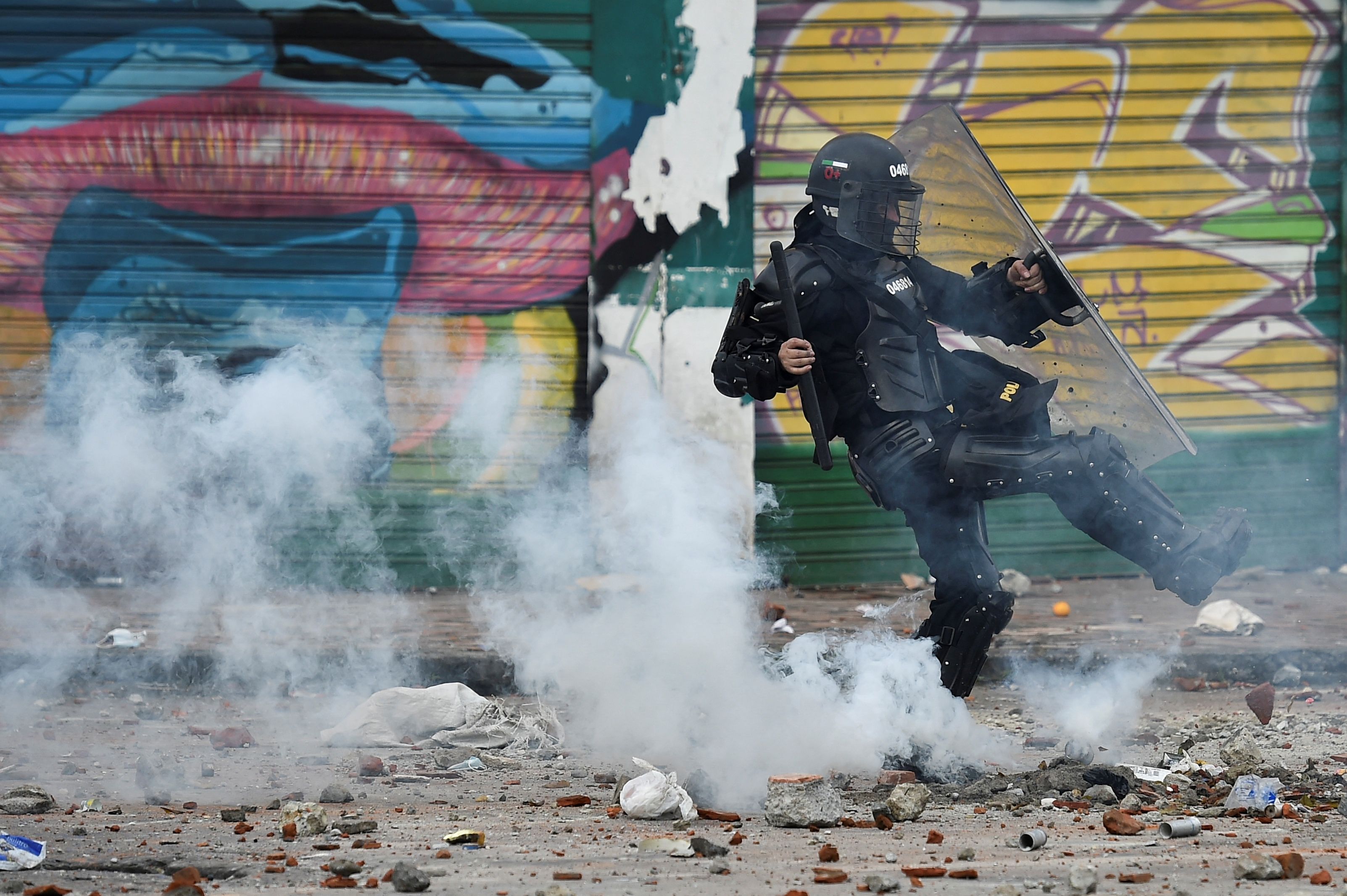 A riot police officer kicks a tear gas canister at demonstrators during a protest against a proposed government tax reform in Cali, Colombia, on May 3, 2021. - Protesters in Colombia on May 3 called for a new mass rally after 19 people died and more than 800 were wounded in clashes during five days of demonstrations against a proposed government tax reform. Faced with the unrest, the government of President Ivan Duque on May 2 ordered the tax reform proposal be withdrawn from Congress, where it was being debated. (Photo by Luis ROBAYO / AFP)