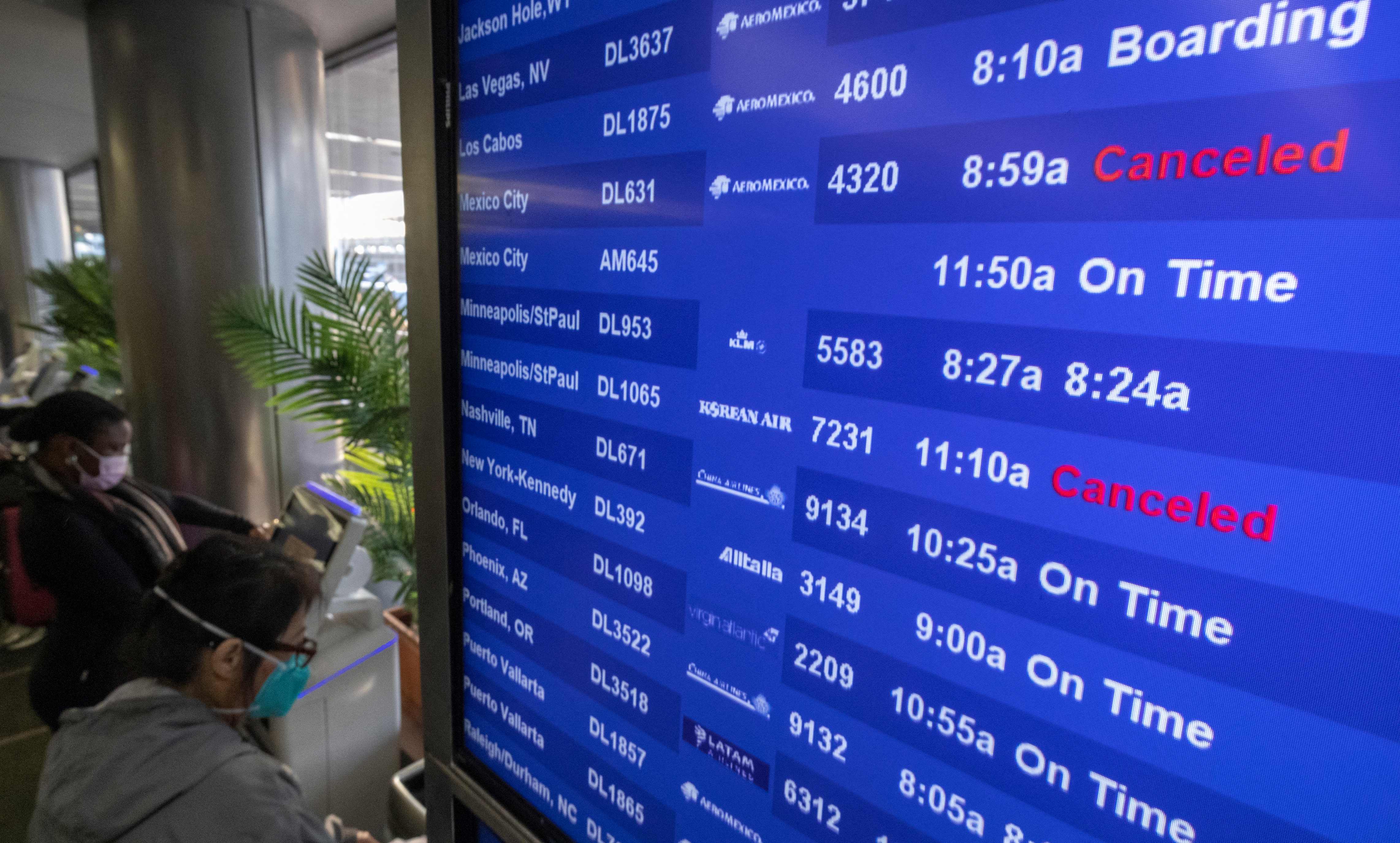 Travelers check for flight information at Los Angeles International Airport in Los Angeles, California, on December 23, 2021. - Over 2,000 flights have been cancelled and thousands delayed around the world as the highly infectious Omicron variant disrupts holiday travel. According to tracking website Flightaware.com at 1540 GMT on Friday, a total of 2,118 flights had been cancelled worldwide, including 500 flights originating from or headed to US airports, and over 5,700 delayed. (Photo by DAVID MCNEW / AFP)