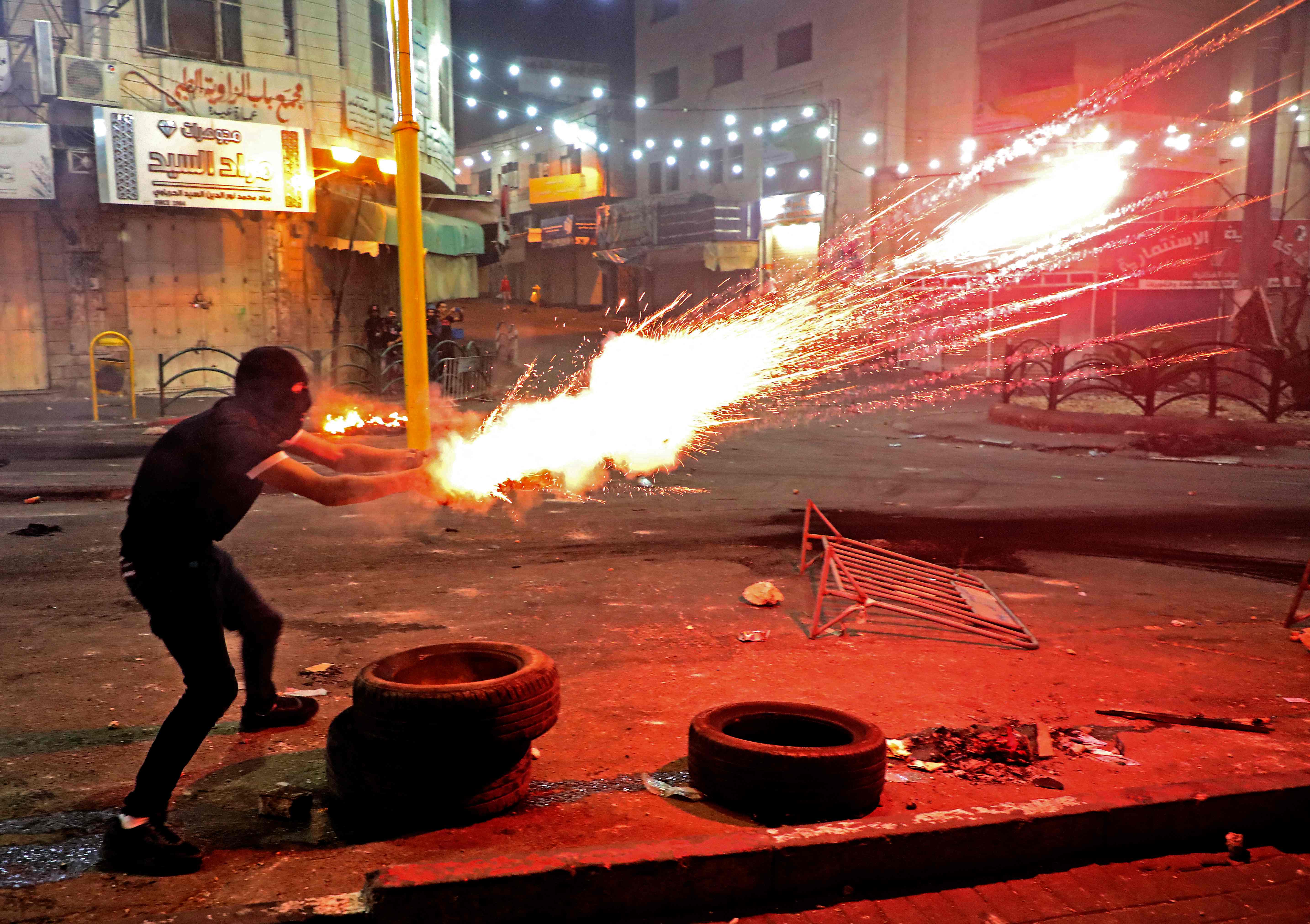 A Palestinian protester launches flares amid clashes with Israeli soldiers in the city center of Hebron in the occupied West Bank, following a rally for Fateh movement supporters denouncing the Israeli Gaza attacks and supporting Palestinians of Jerusalem, on May 14, 2021. (Photo by HAZEM BADER / AFP)