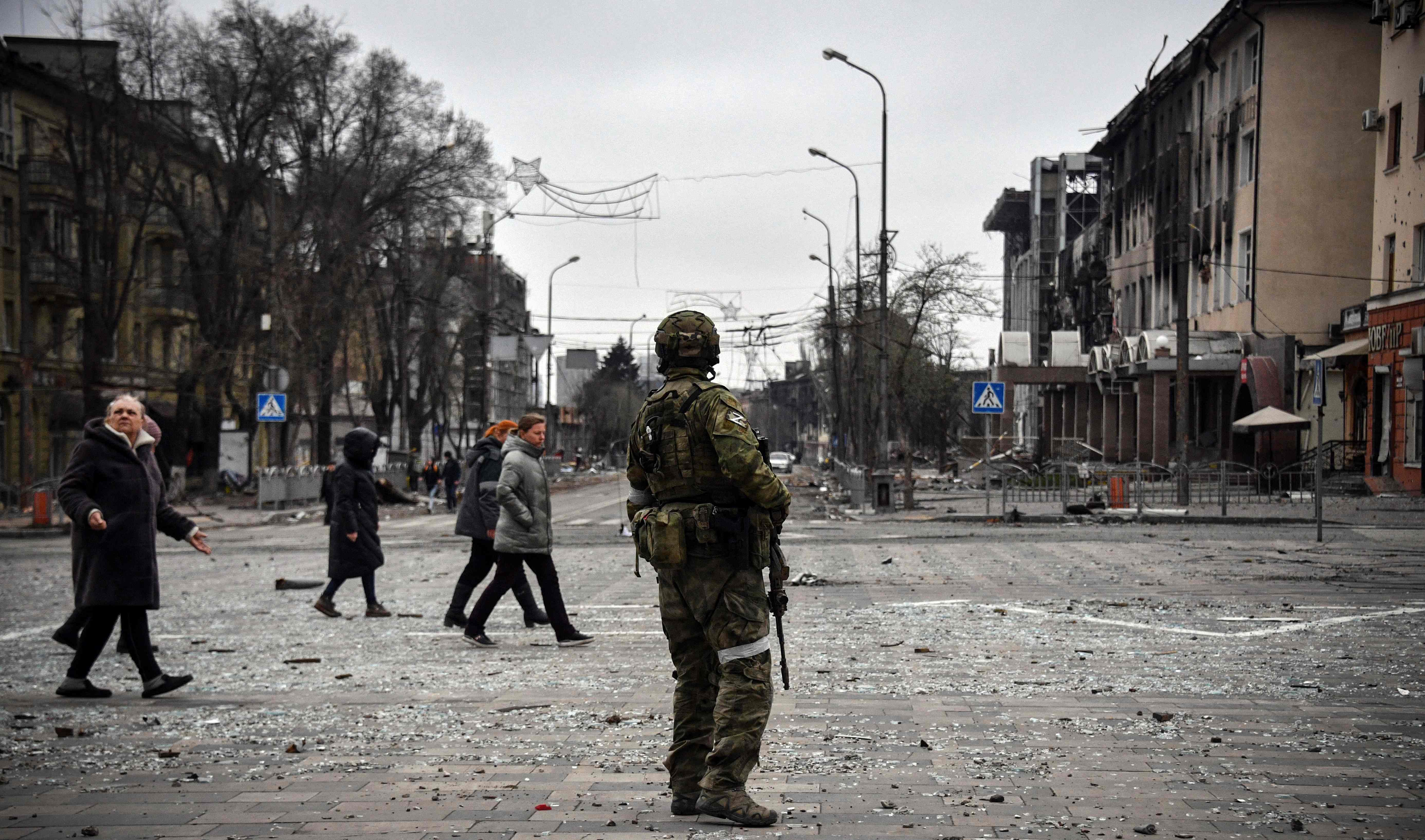 TOPSHOT - People pass by a Russian soldier in central Mariupol on April 12, 2022, as Russian troops intensify a campaign to take the strategic port city, part of an anticipated massive onslaught across eastern Ukraine, while Russia's President makes a defiant case for the war on Russia's neighbour. - *EDITOR'S NOTE: This picture was taken during a trip organized by the Russian military.* (Photo by Alexander NEMENOV / AFP)