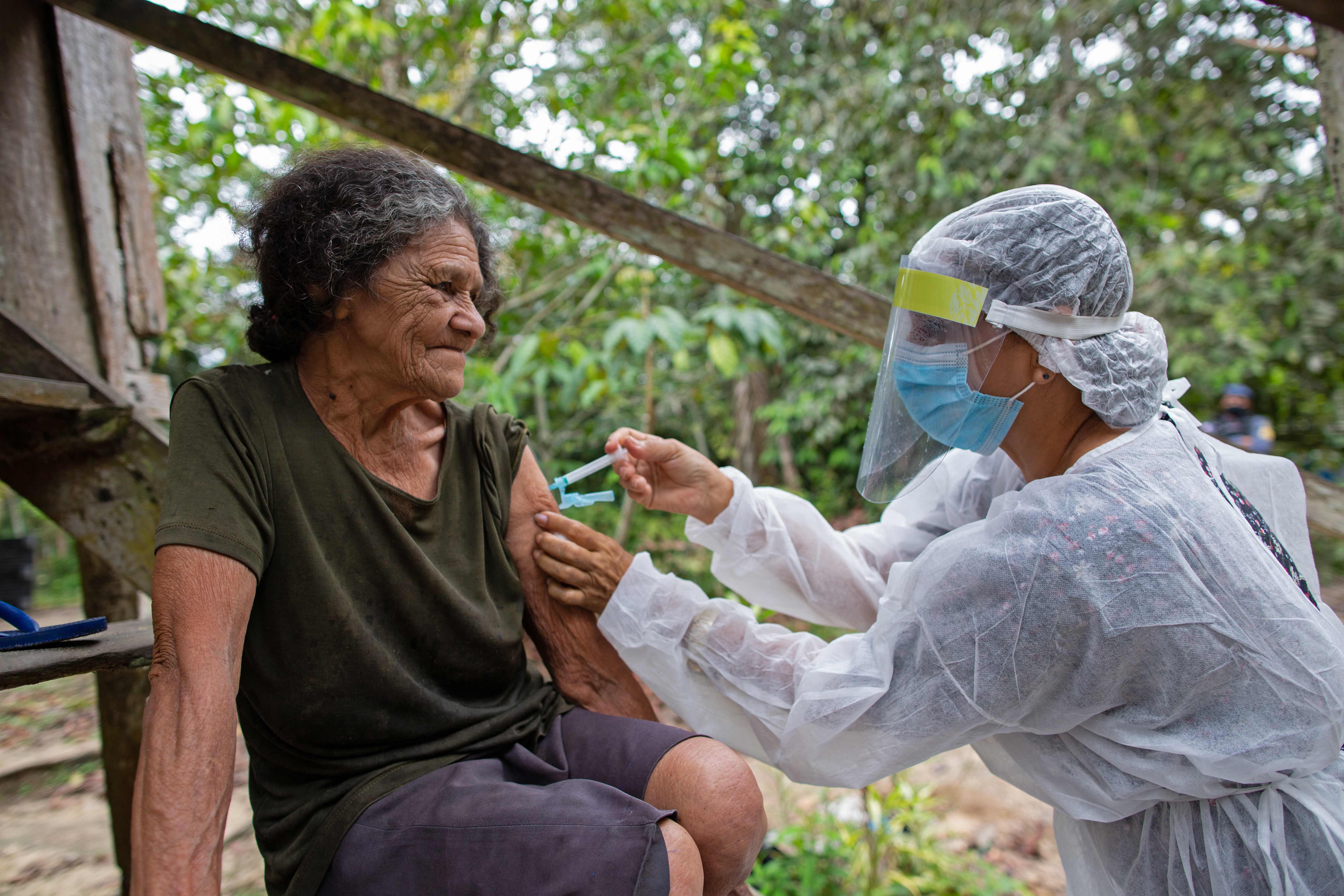 (FILES) In this file photo taken on February 09, 2021 Maria Ferreira, 74, is vaccinated by a health worker with a dose of Oxford-AstraZeneca COVID-19 vaccine in the Nossa Senhora Livramento community on the banks of the Rio Negro near Manaus, Amazonas state, Brazil. (Photo by MICHAEL DANTAS / AFP)
