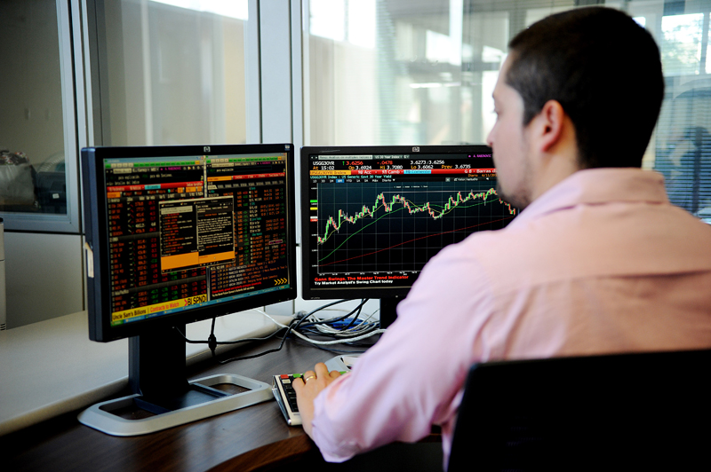Hombre con camisa rosada analiza en su computadora datos financieros y gráficos de inversión en la bolsa de valores.