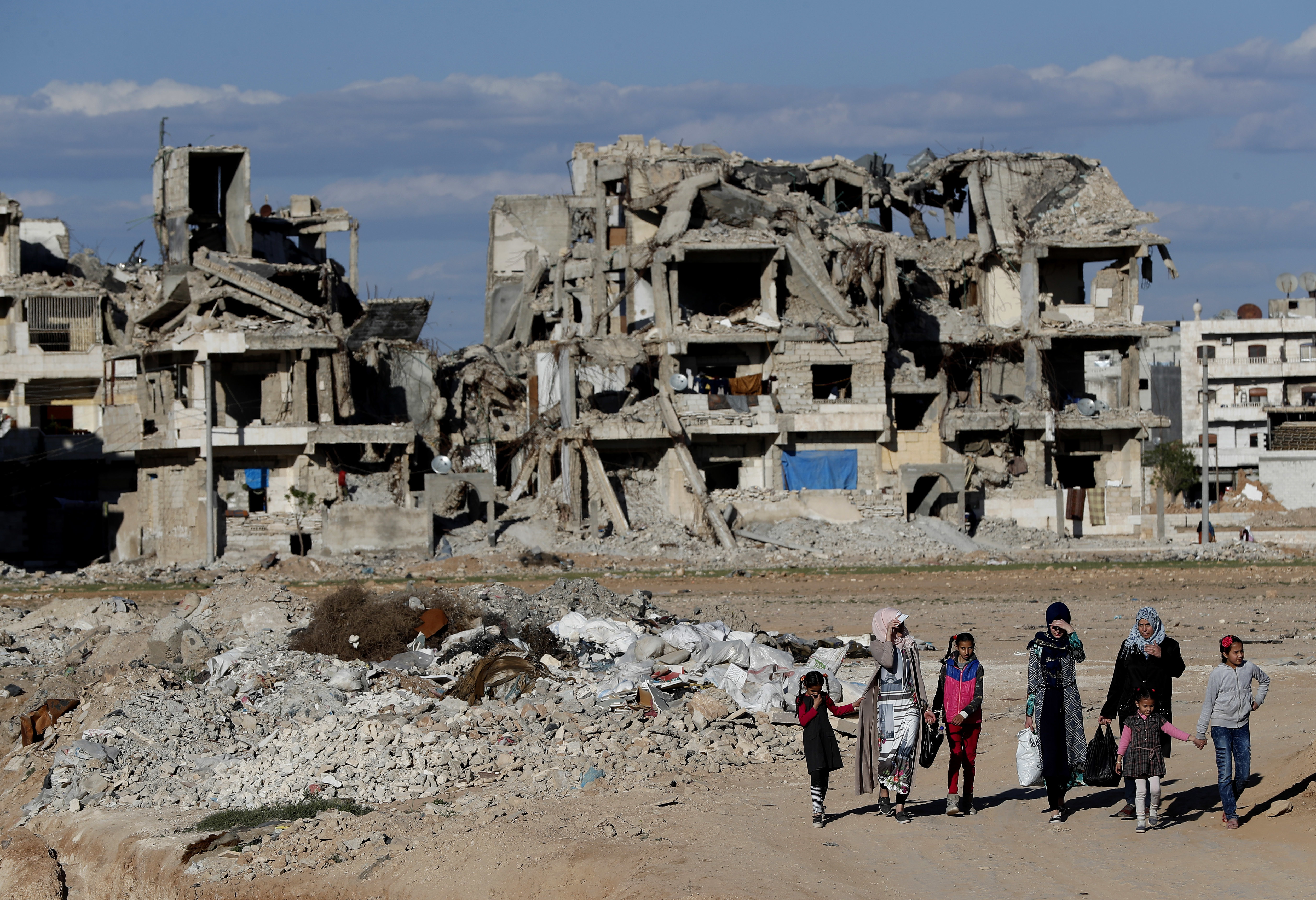 In this March 31, 2018 photo, Syrian citizens walk in front of buildings that were destroyed during the battle between the U.S.-backed Syrian Democratic Forces fighters and Islamic State militants, in Manbij, north Syria. On Friday, Dec. 28, 2018, Syria’s military said it entered the flashpoint Kurdish-held town of Manbij, where Turkey has threatened an offensive -- a claim that was refuted by U.S. troops who patrol the town. The announcement and the conflicting reports reflect the potential for chaos in the wake of the U.S. surprise decision to withdraw troops from Syria (AP Photo/Hussein Malla)