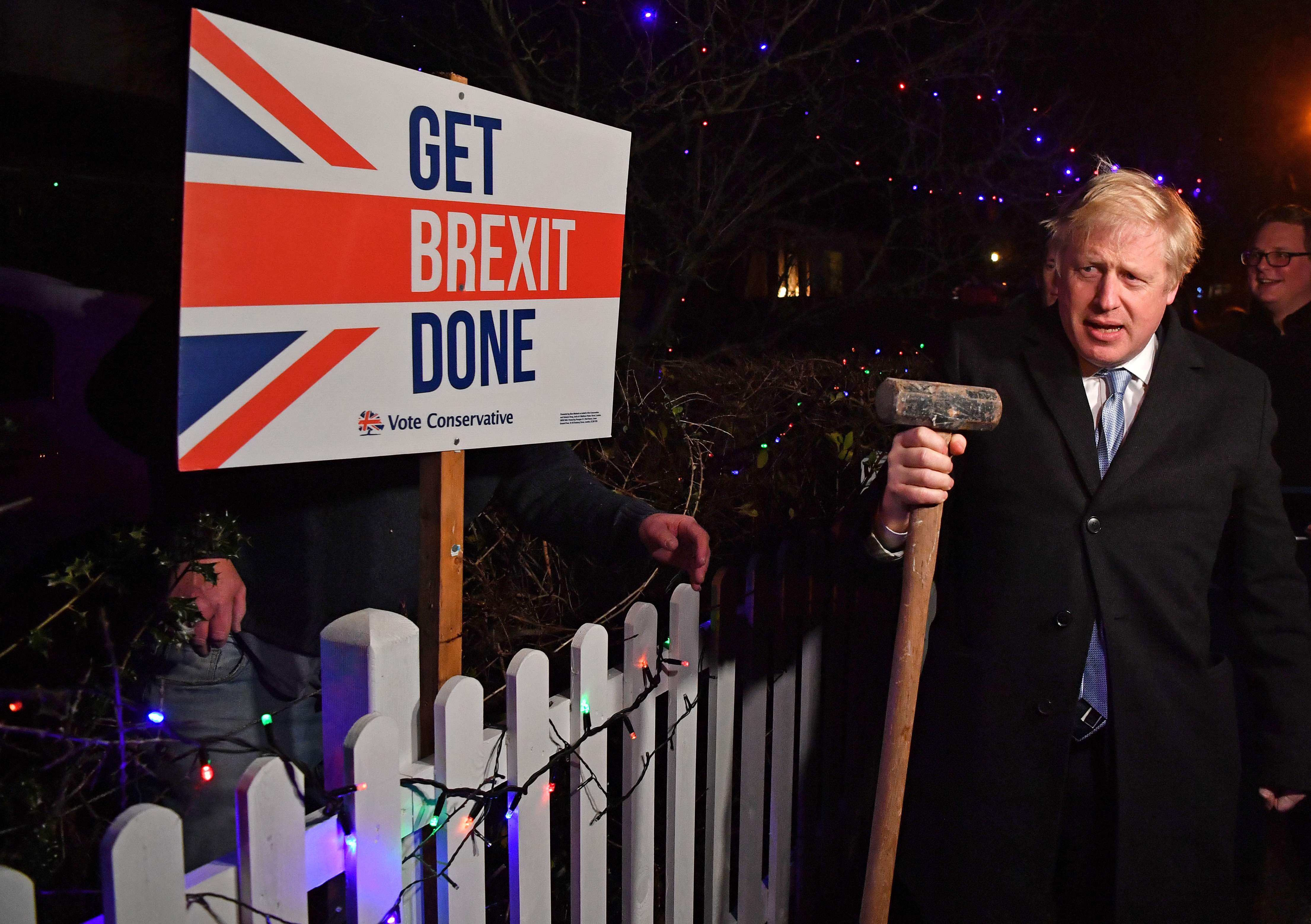 Britain's Prime Minister and Conservative party leader Boris Johnson poses after hammering a "Get Brexit Done" sign into the garden of a supporter, with a sledgehammer as he campaigns with his team in Benfleet, east of London on December 11, 2019, the final day of campaigning for the general election. - Britain will go to the polls tomorrow to vote in a pre-Christmas general election. (Photo by Ben STANSALL / POOL / AFP)