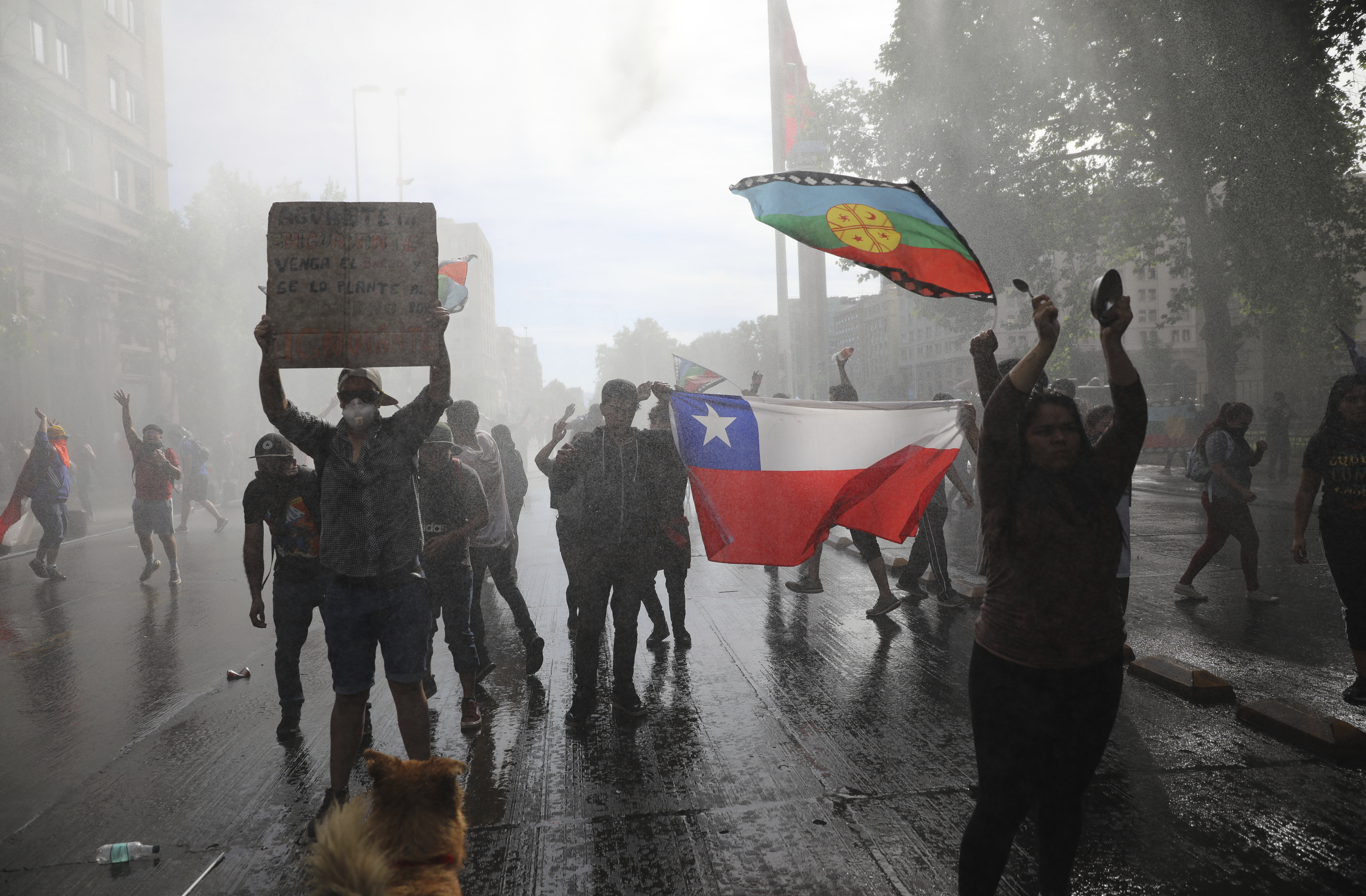 Anti-government demonstrators are sprayed by a police water cannon during a protest in Santiago, Chile, Saturday, Oct. 26, 2019. Chile has been facing days of unrest, triggered by a relatively minor increase in subway fares. The protests have shaken a nation noted for economic stability over the past decades, which has seen steadily declining poverty despite persistent high rates of inequality. (AP Photo/Rodrigo Abd)