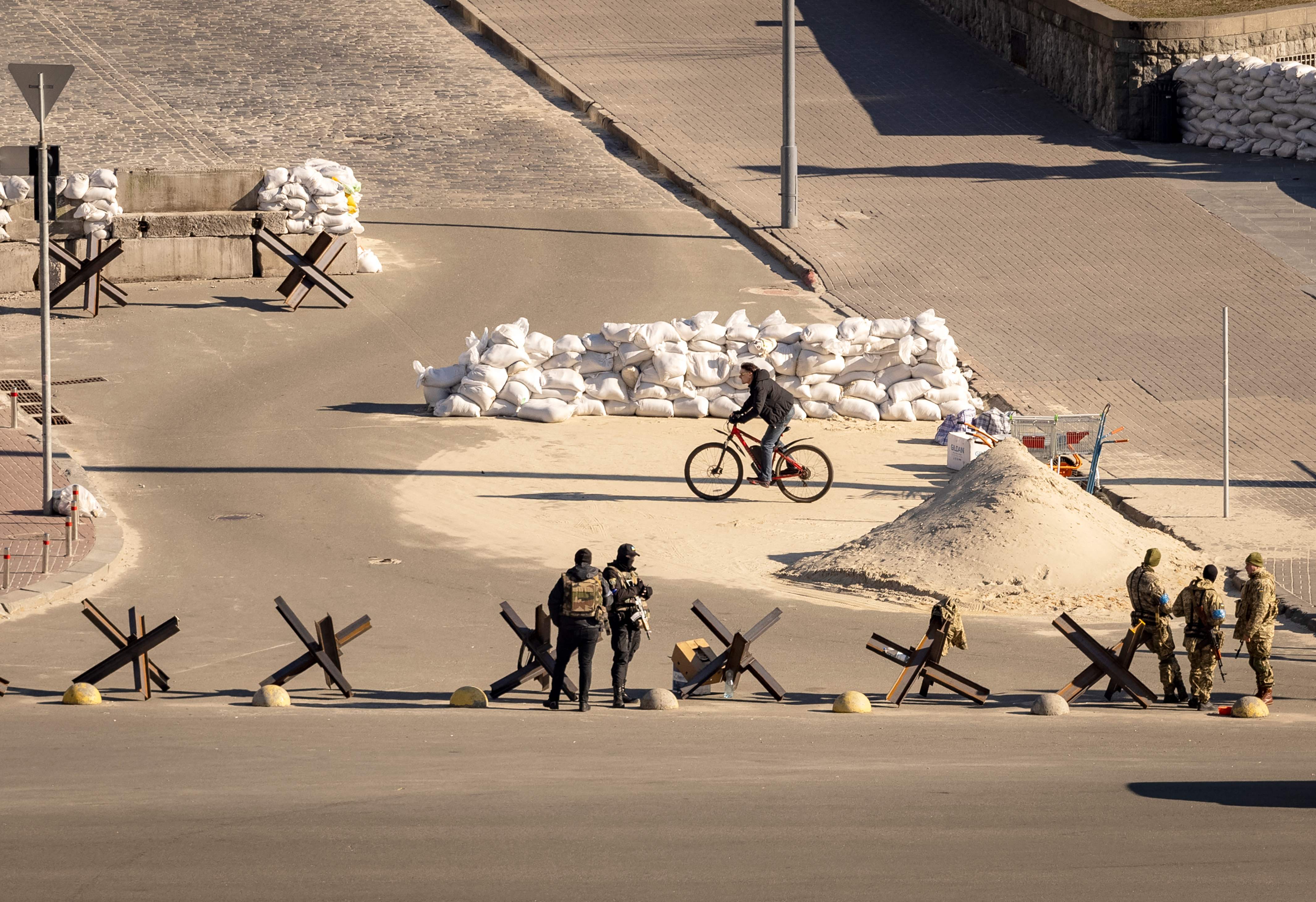 TOPSHOT - A cyclist rides past Ukrainian servicemen standing guard at a military check point in the center of Kyiv on March 15, 2022, on the 20th day of the Russian invasion of Ukraine. - Russian and Ukrainian delegations resumed talks on Maarch 15, 2022, as Russian strikes on Kiev increased and the Russian offensive spread across the country, sending more than three million Ukrainians into exile. (Photo by FADEL SENNA / AFP)