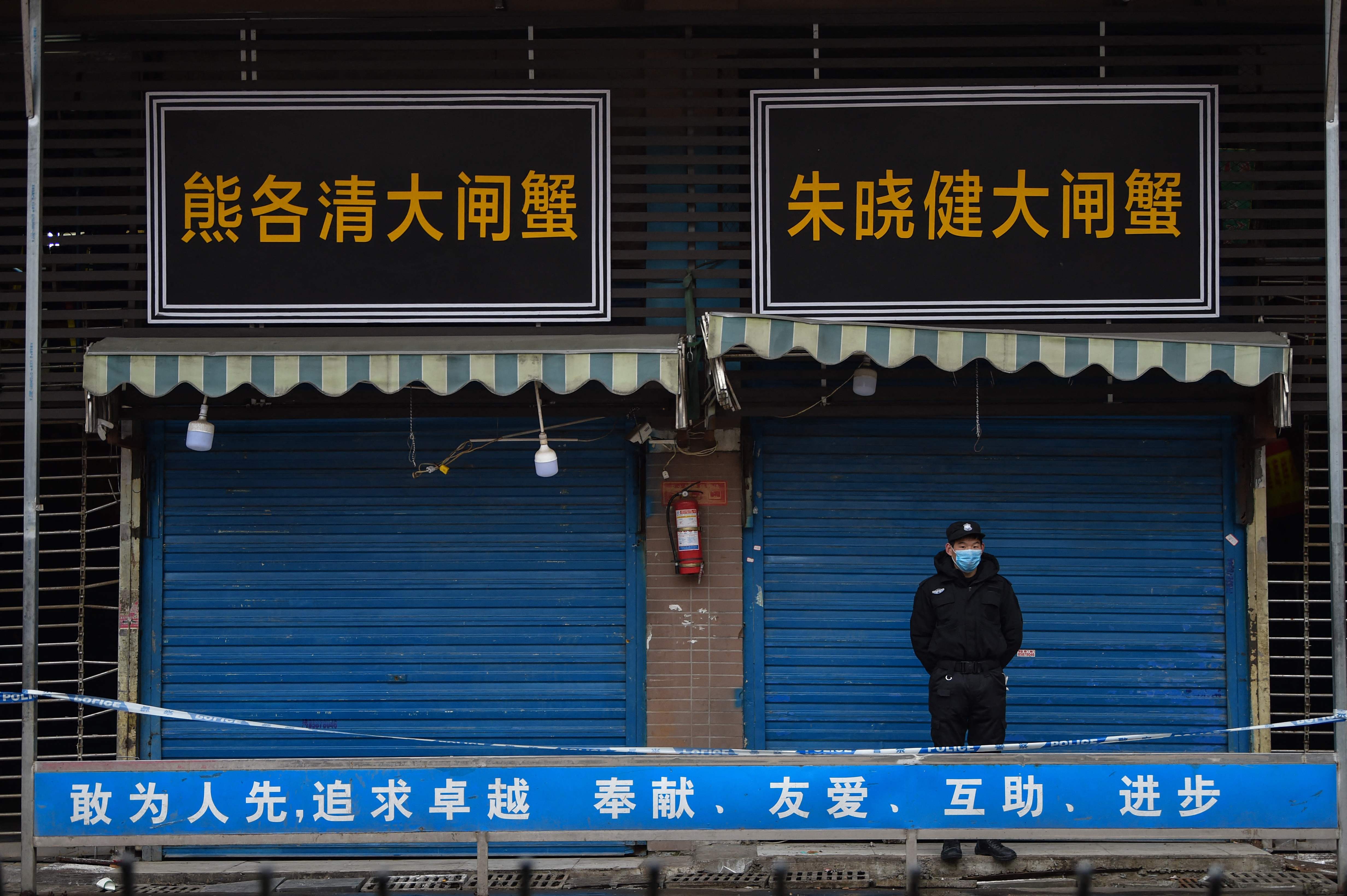 (FILES) In this file photo taken on January 24, 2020 a security guard stands outside the Huanan Seafood Wholesale Market where the coronavirus was detected in Wuhan. - An international expert mission to Wuhan has concluded that it was very likely that Covid first passed to humans from a bat through an intermediary animal, while all but ruling out a lab incident. The experts said that the intermediary host hypothesis was deemed "likely to very likely", while the theory that the virus escaped from a laboratory was seen as "extremely unlikely", according to the final version of the long-awaited report, of which AFP obtained a copy on March 29, 2021 before the official release. (Photo by Hector RETAMAL / AFP)