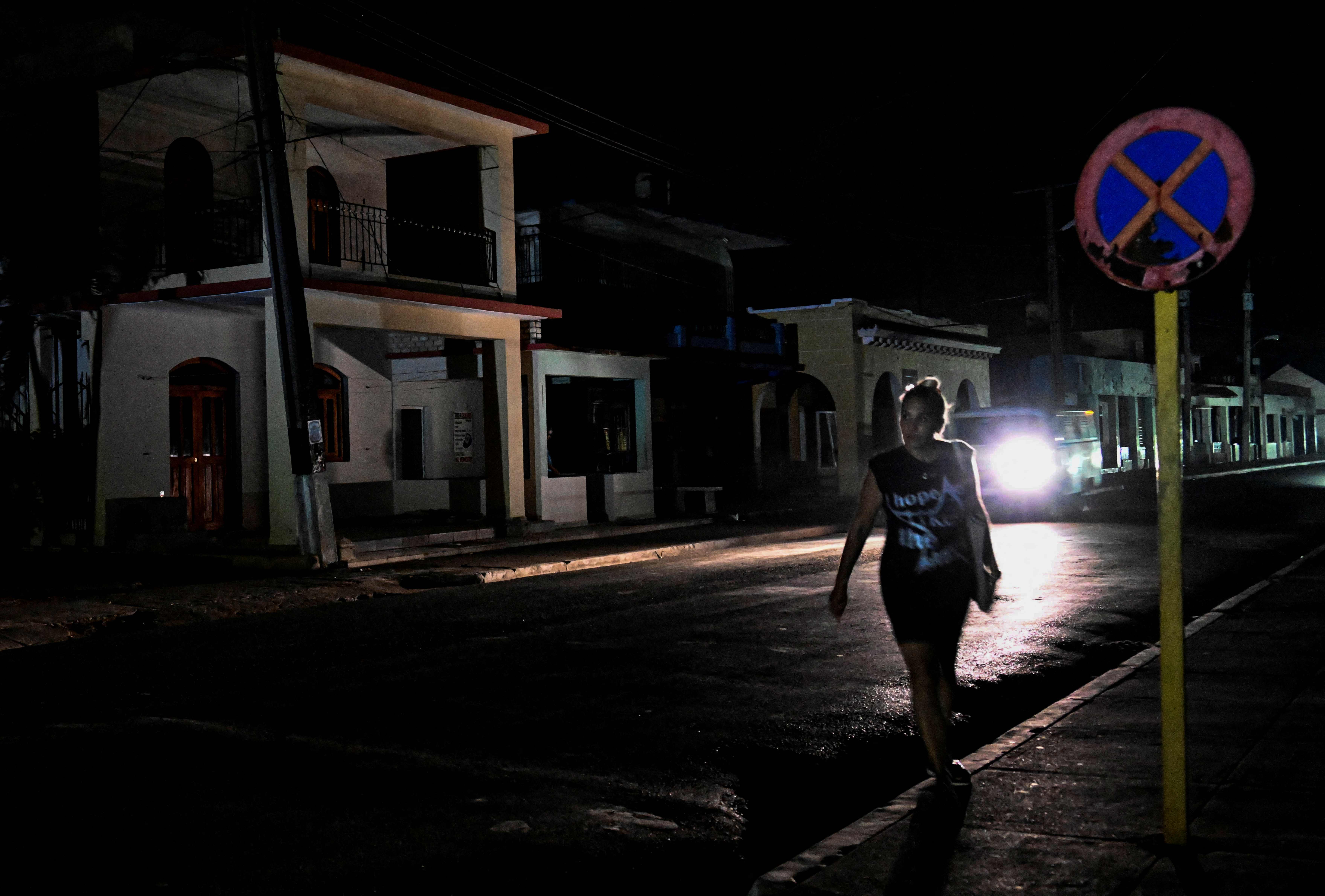 A woman walks down a dark street during a blackout in the Bauta municipality, Artemisa province, Cuba, on March 18, 2024. (Photo by YAMIL LAGE / AFP)