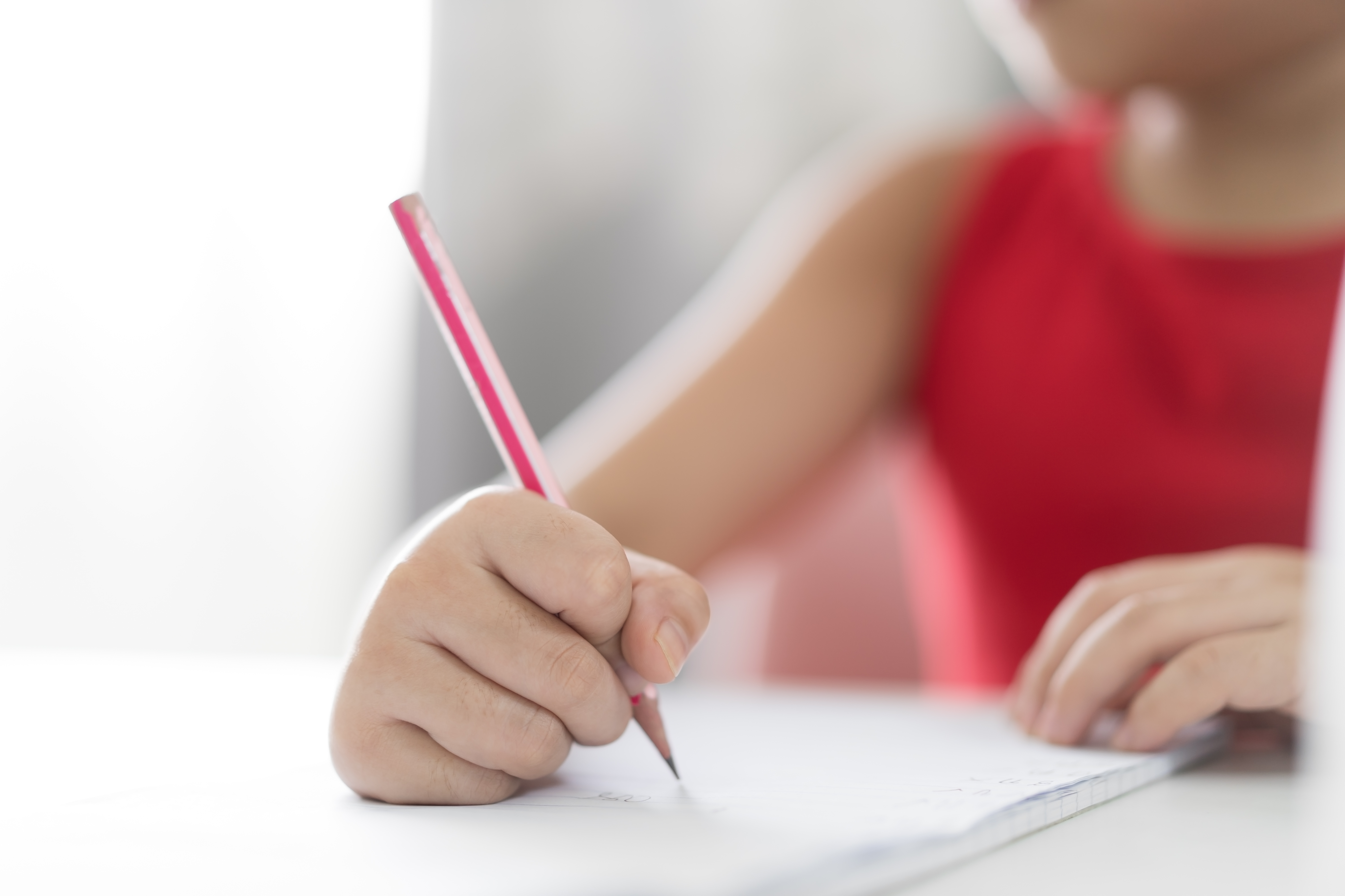 Se ve la mano y parte del tronco de una niña o adolescente escribiendo en un papel blanco.