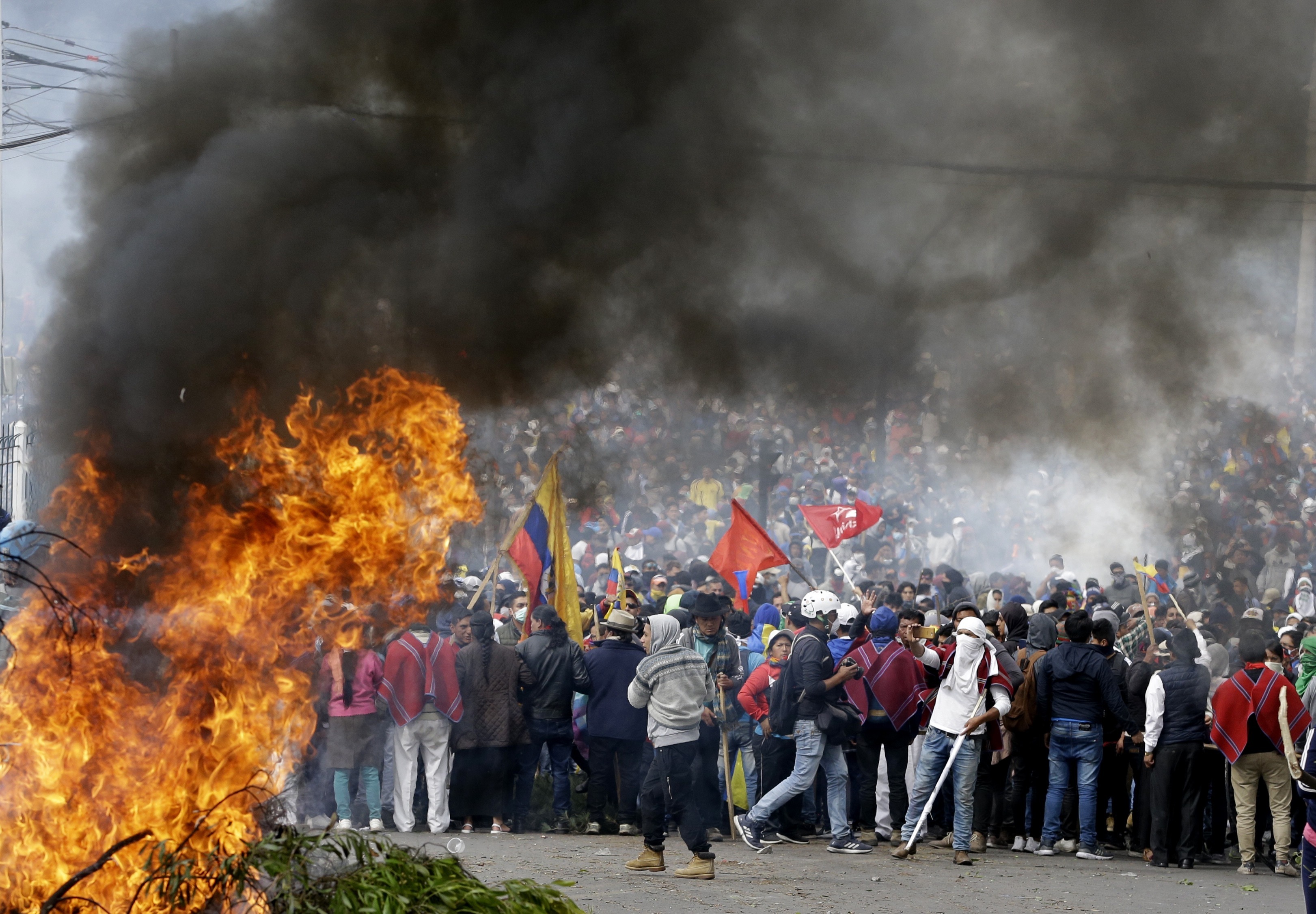 Anti-government demonstrators gather behind a burning barricade during a protest against President Lenin Moreno and his economic policies, in Quito, Ecuador, Tuesday, Oct. 8, 2019. Ecuador has endured days of popular upheaval since President Moreno scrapped fuel price subsidies, a step that set off protests and clashes across the South American country. (AP Photo/Fernando Vergara)