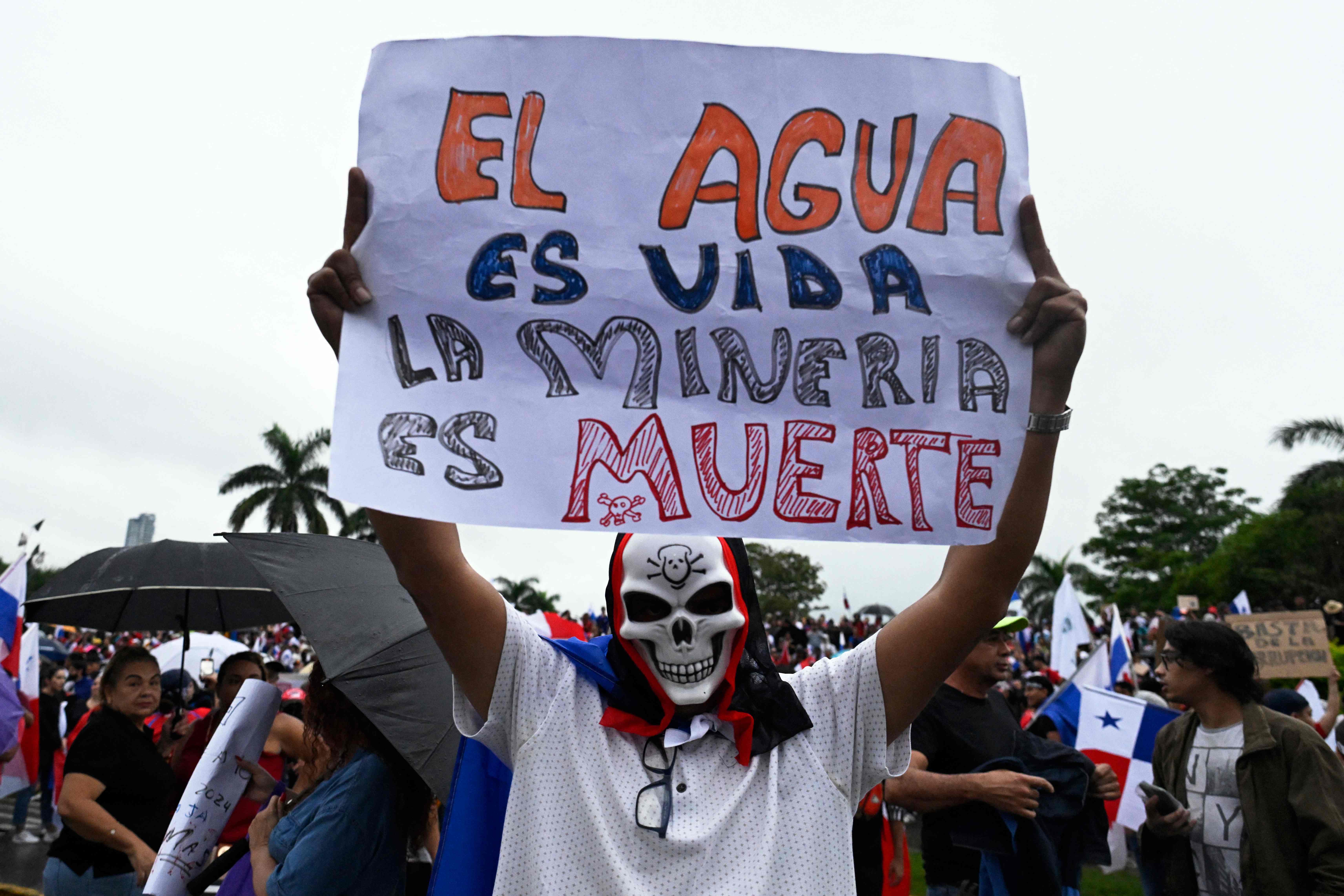 TOPSHOT - A demonstrator holds a sign reading "Water is life, Mining is death" during a protest against the government contract with Canadian mining company First Quantum -and its subsidiary Minera Panama- in Panama City, Panama on October 26, 2023. In 2021, Panama's Supreme Court ratified a lower court's ruling that the original concession of mining rights granted to subsidiary Minera Panama until 2037 was unconstitutional, but negotiations between the government and First Quantum led to a new contract through which the company will pay the government ten times more than previously and is allowed to operate in Panama for 20 years, renewable for another two decades. (Photo by LUIS ACOSTA / AFP)