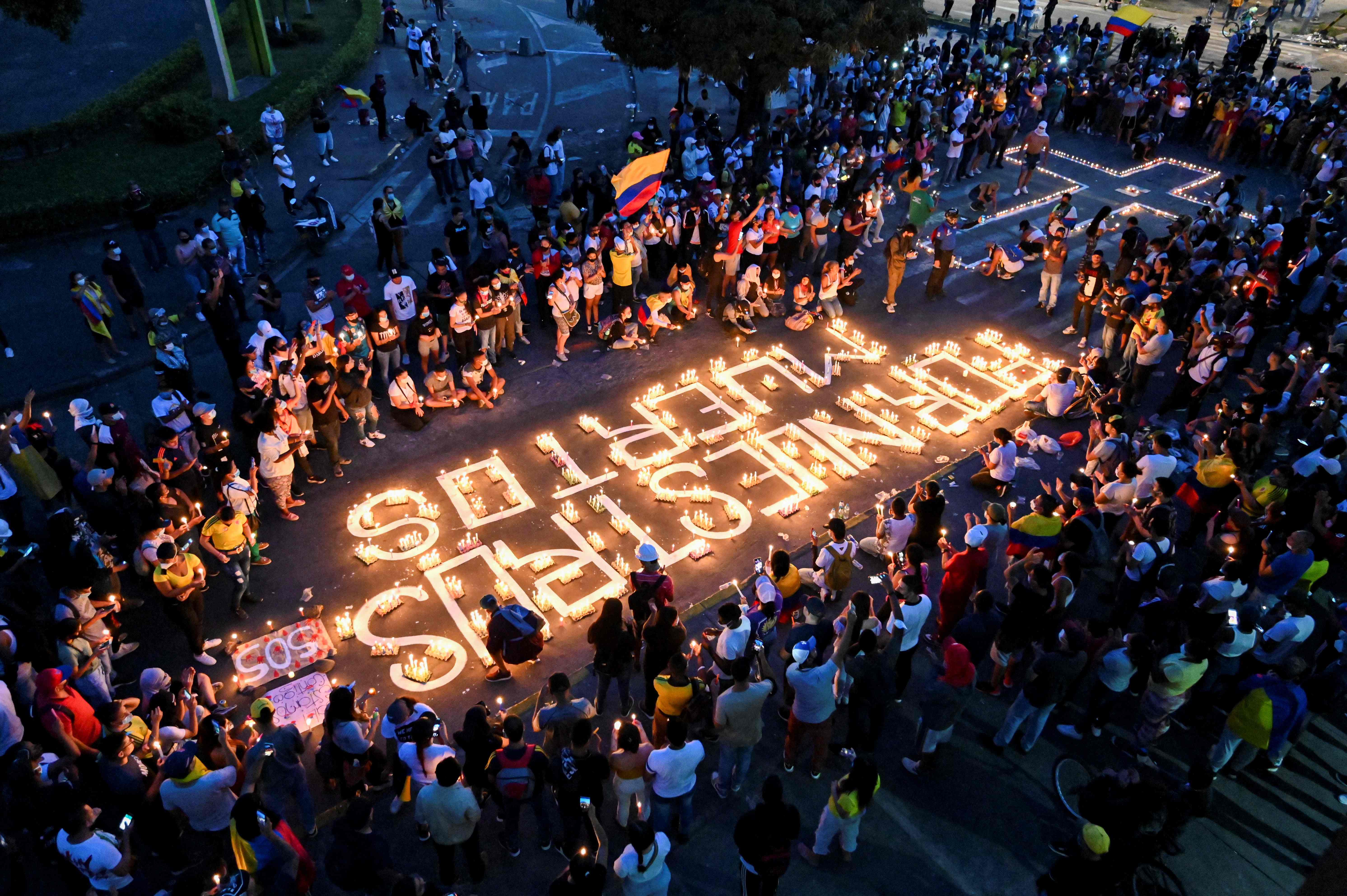 TOPSHOT - People gather around candles and words on the pavement reading "for our dead" during a vigil on May 5, 2021 in Cali, Colombia, in honor of the demonstrators who died during protests against the government of President Ivan Duque. - Thousands of people returned to the streets of Colombia on May 5 in rejection of the government of Ivan Duque, who has completed a week of pressure with demonstrations that turned violent in some cities and left some twenty people dead. (Photo by Luis ROBAYO / AFP)