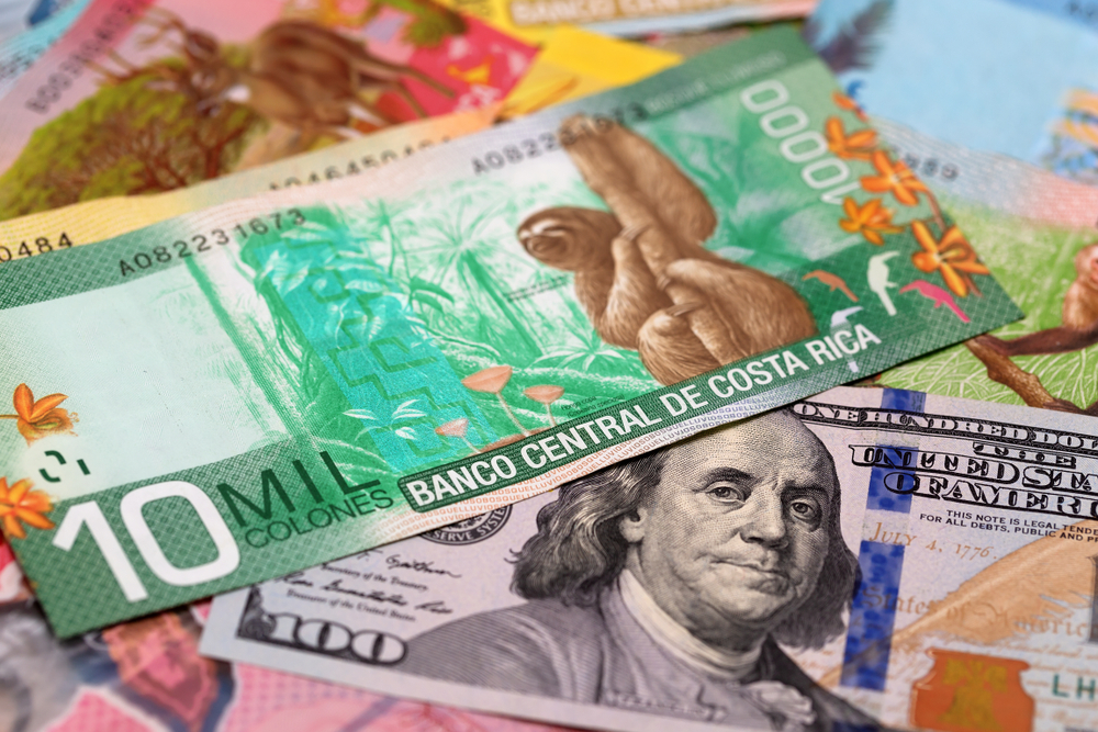 Primer plano de billetes de ¢10.000 y $100, representando la inversión en colones y dólares ofrecida por el CDP Tasa TRI del BCR.
