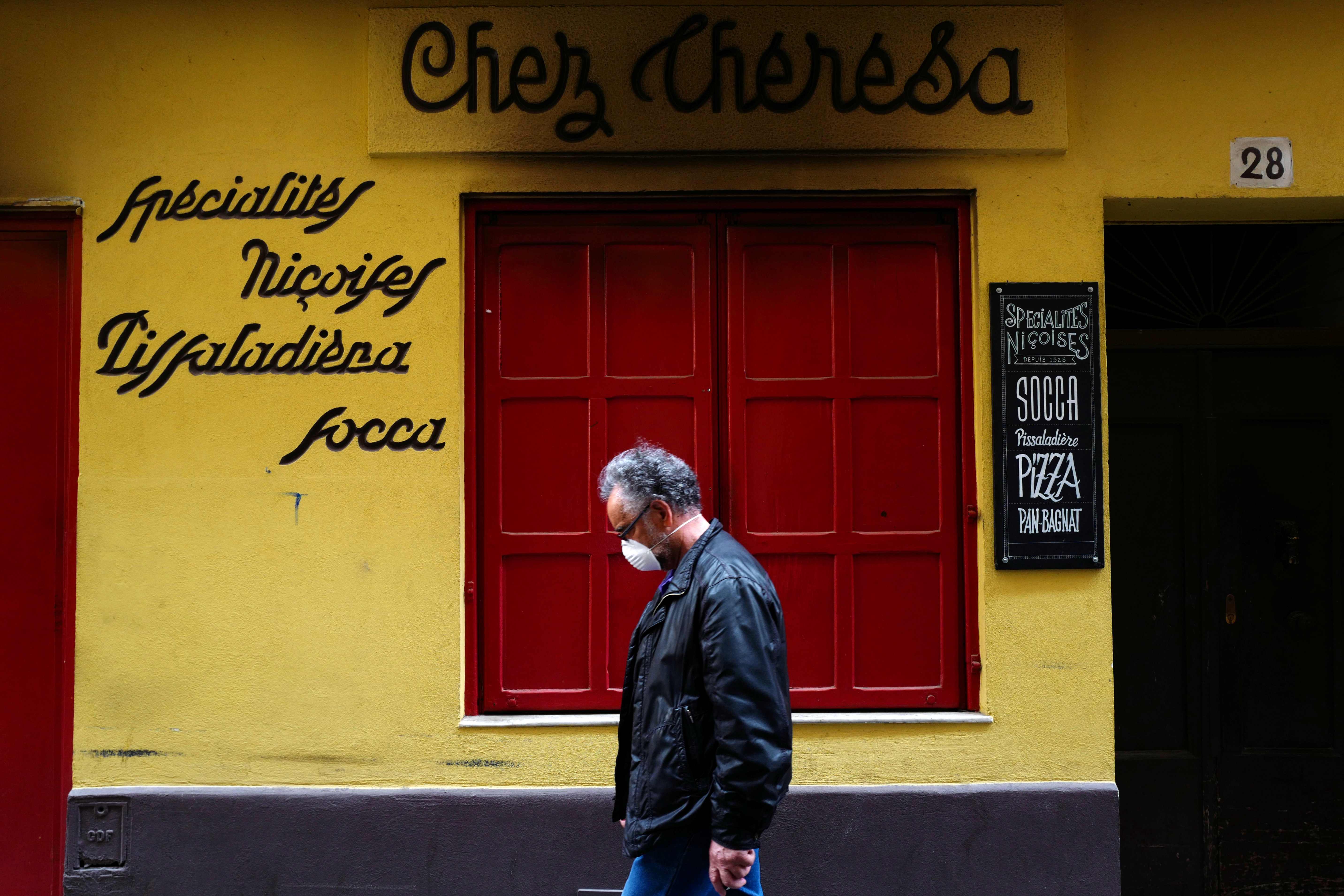 A man wearing a face mask walks past a closed restaurant in an empty street in the French Riviera city of Nice, southern France, on May 9, 2020, on the 54th day of a lockdown in France aimed at curbing the spread of the COVID-19 pandemic, the novel coronavirus. (Photo by VALERY HACHE / AFP)