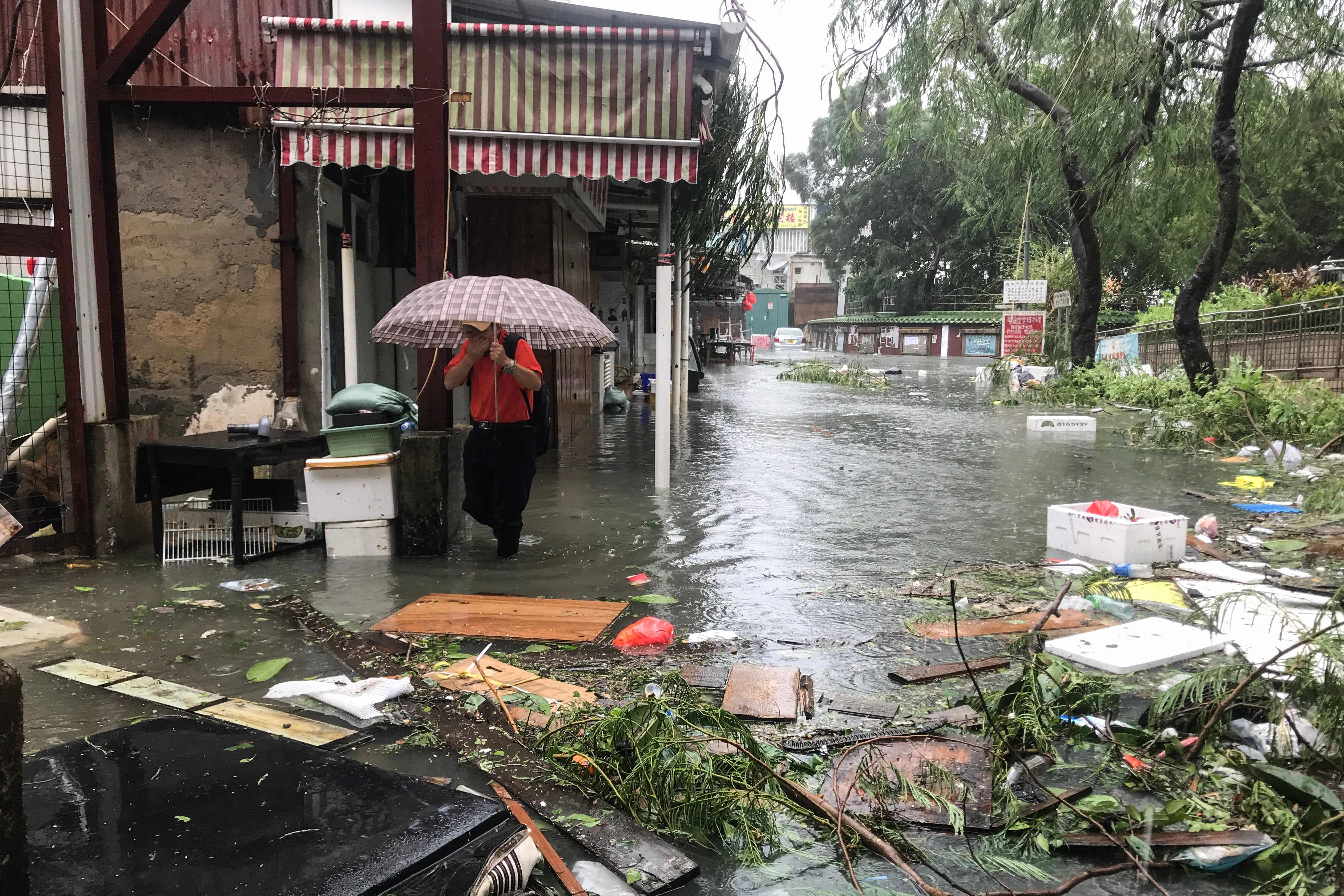 Un hombre trata de protegerse de la lluvia mientras camina por una zona inundada en el pueblo pesquero de Lei Yu Mun, en Hong Kong. Foto: AFP