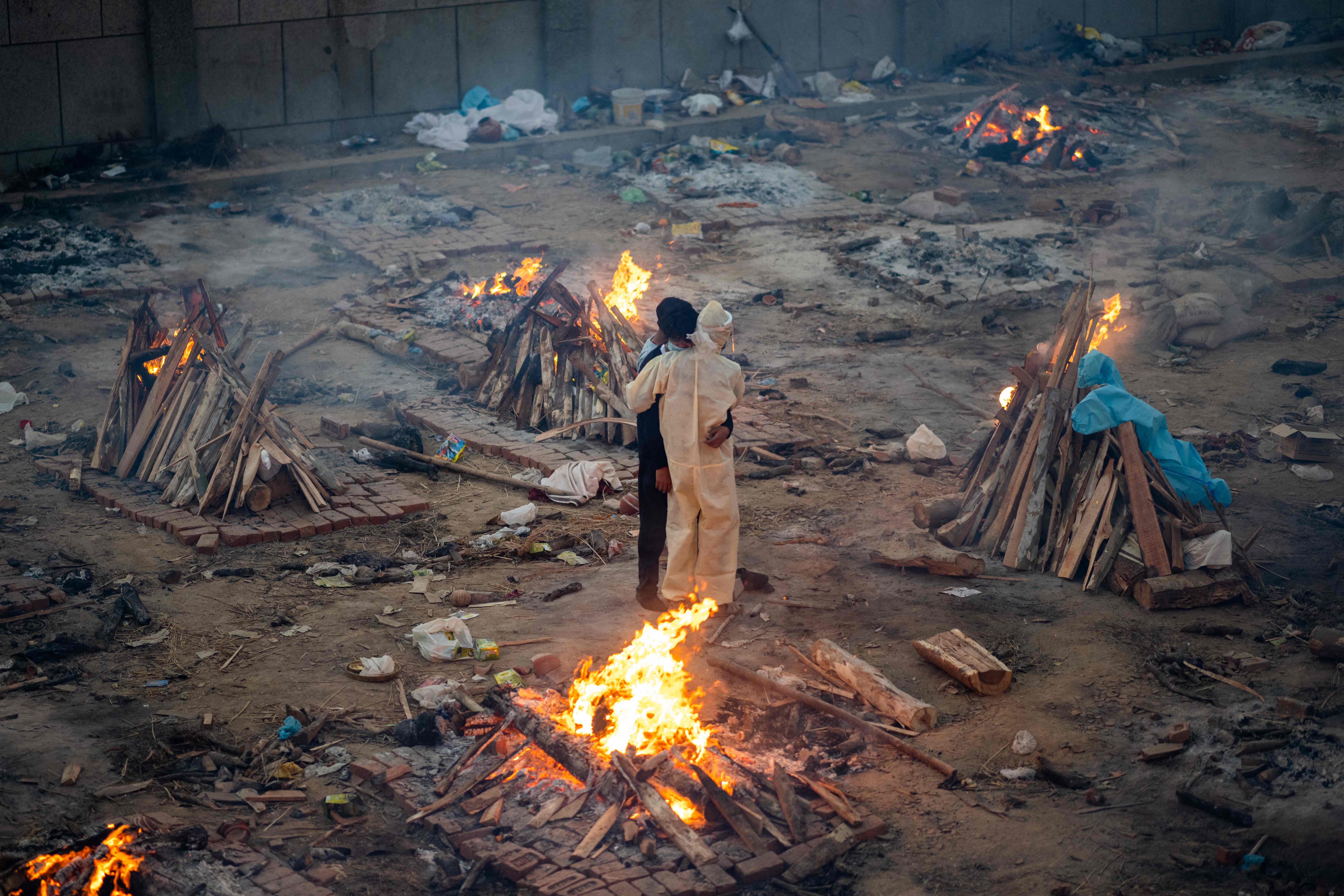Family members embrace each other amid burning pyres of victims who lost their lives due to the Covid-19 coronavirus at a cremation ground in New Delhi on April 26, 2021. (Photo by Jewel SAMAD / AFP)