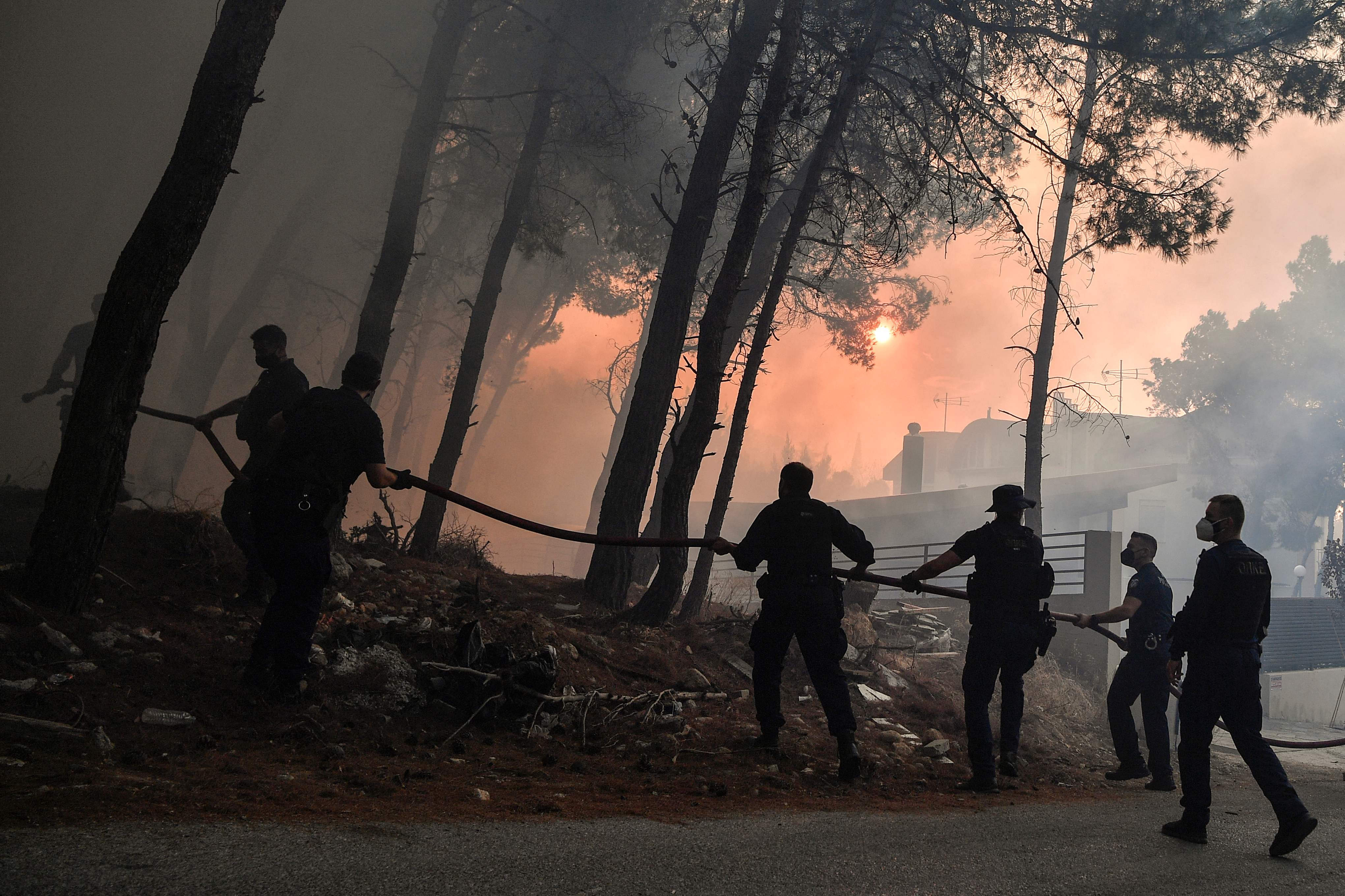 Police officers help firefighters to extinguish a fire in Thrakomakedones, near Mount Parnitha, north of Athens, on August 7, 2021. - Hundreds of firefighters battled a blaze on the outskirts of Athens as several fires raged in Greece. (Photo by Louisa GOULIAMAKI / AFP)