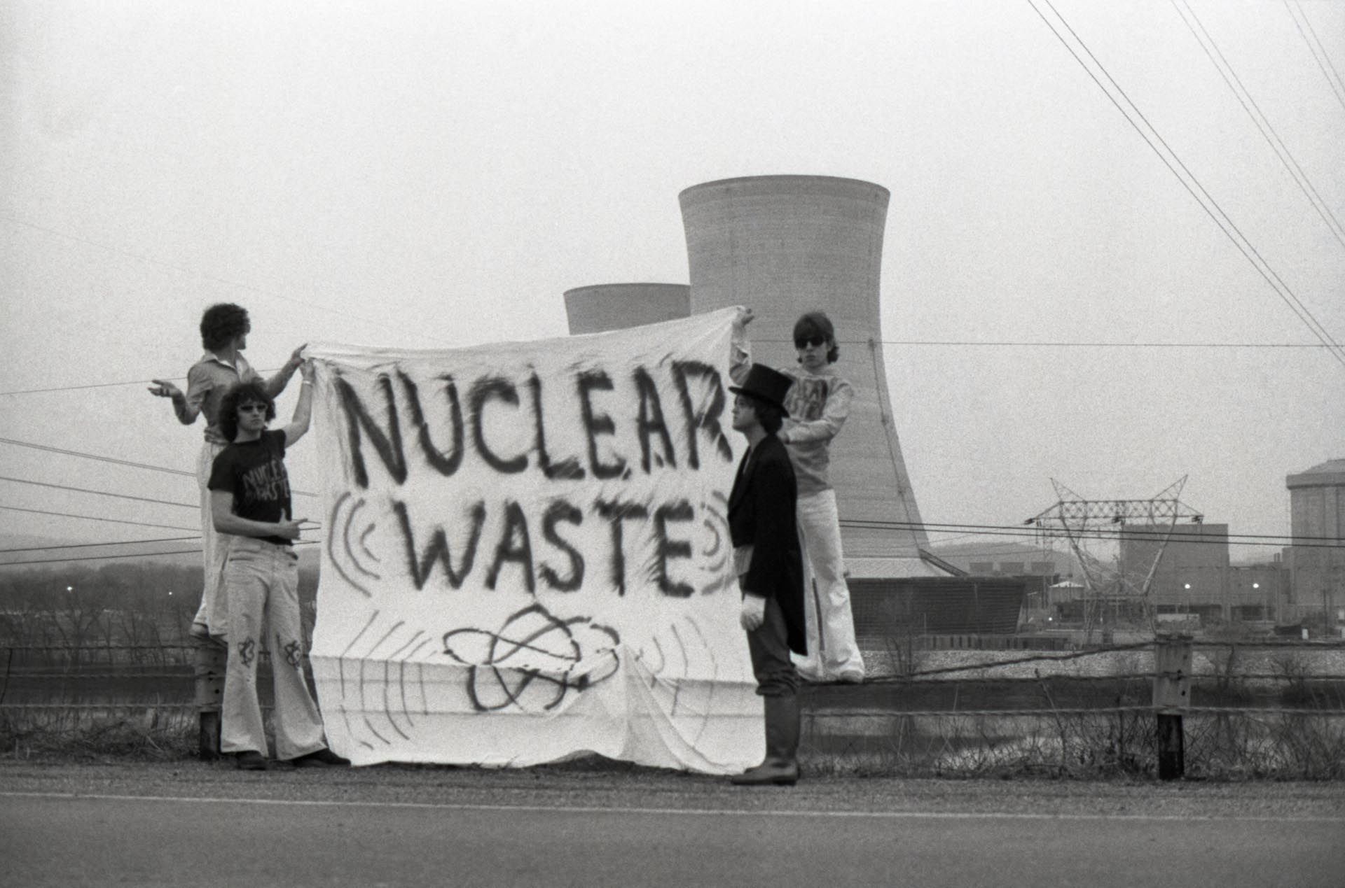 Con un hombre vestido con un traje de enterrador, un grupo de personas desplegó una pancarta de protesta frente a las torres de enfriamiento en la planta nuclear de Three Mile Island (Bettmann Archive)
