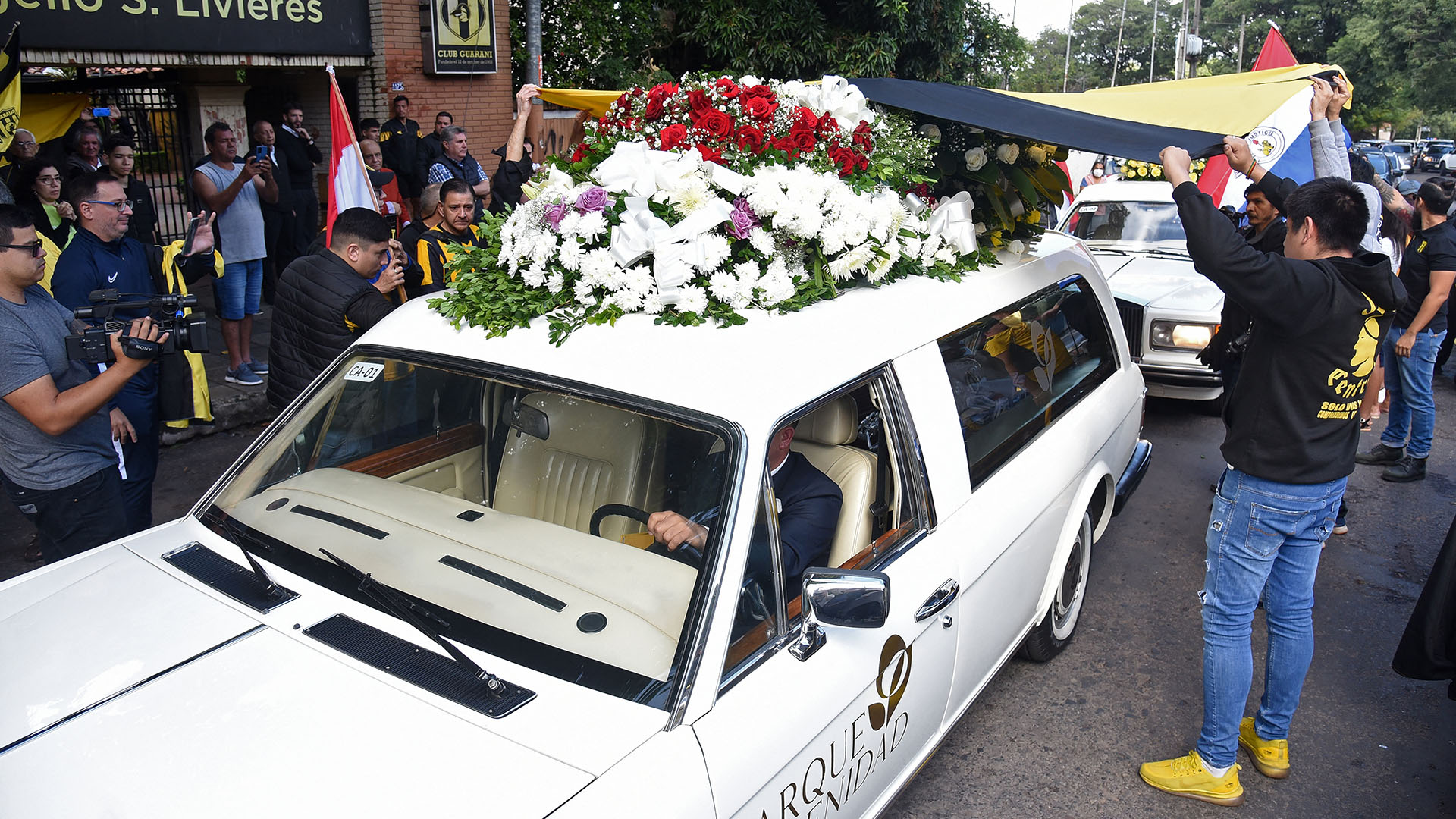 Aficionados del equipo de fútbol paraguayo Guaraní rindieron homenaje al fiscal antidrogas Marcelo Pecci, que también era hincha y miembro de la junta directiva, mientras pasa el coche fúnebre con su ataúd antes de su funeral, en Asunción el 15 de mayo de 2022,  (AFP)