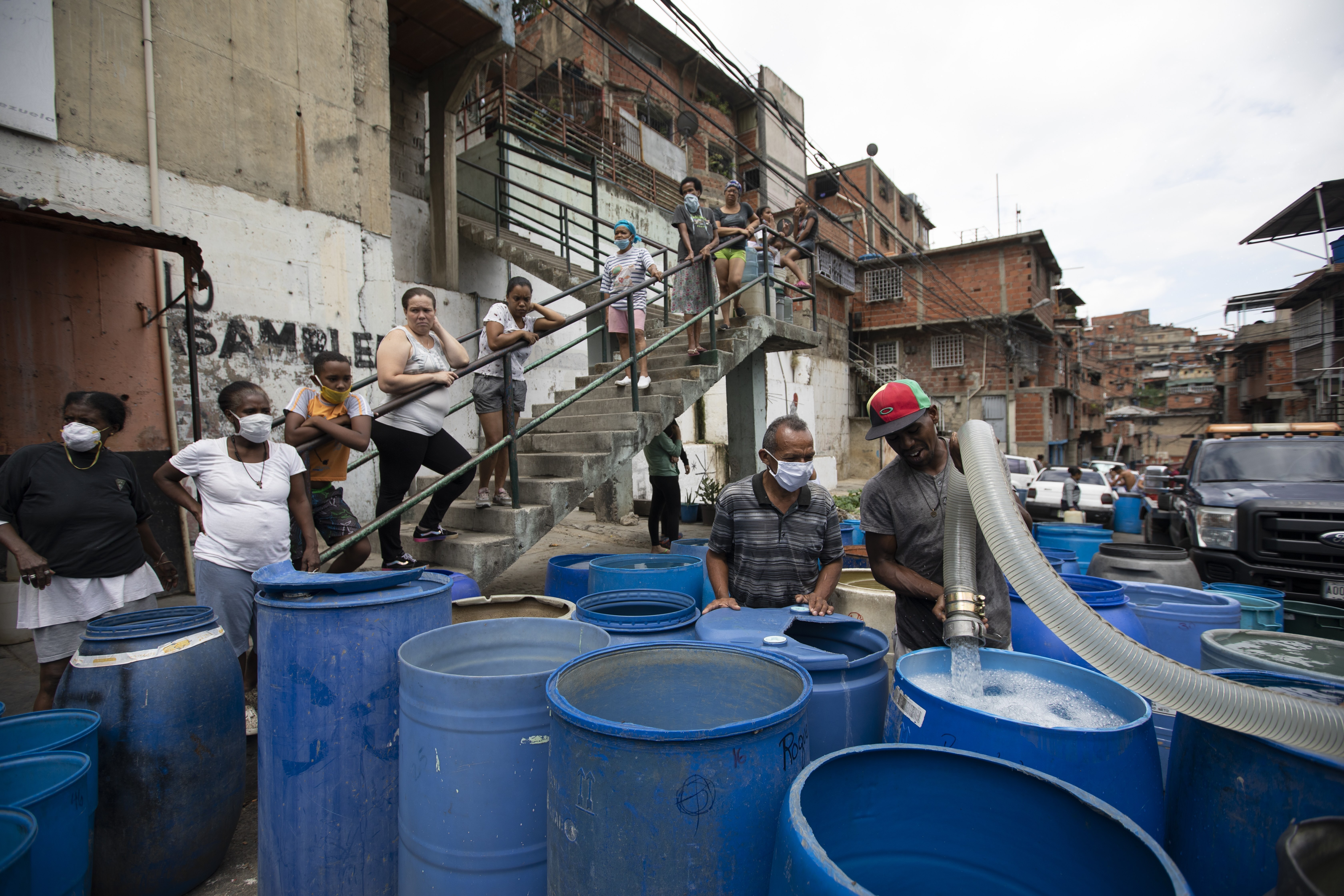 Un residente llena un recipiente con el agua distribuida por un camión cisterna gubernamental en el vecindario de Petare, en Caracas, Venezuela, el 15 de junio de 2020. El gobierno de Nicolás Maduro ha acusado a sus enemigos políticos de sabotear estaciones de bombeo, y recientemente celebró la compra de una flota de 1.000 camiones “súper cisterna” a China para llevar agua a los residentes. (AP Foto/Ariana Cubillos)